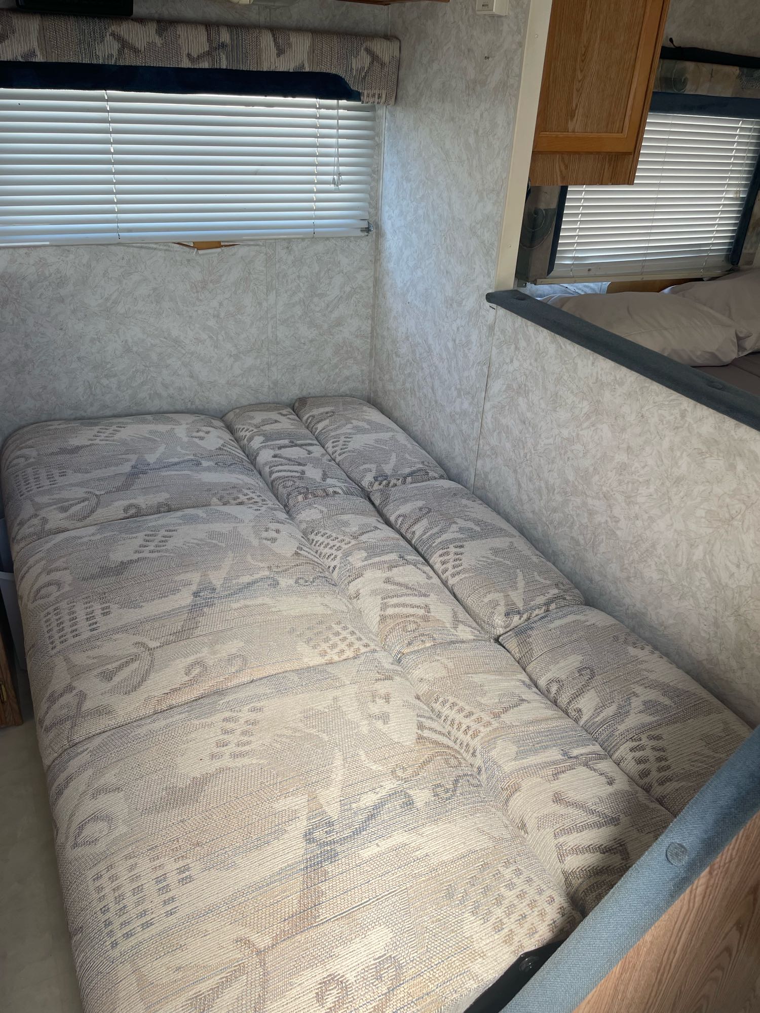 RV rental interior: a modular bed with patterned cushions. Window with white blinds and light textured walls visible.. Thor Wanderer 2001