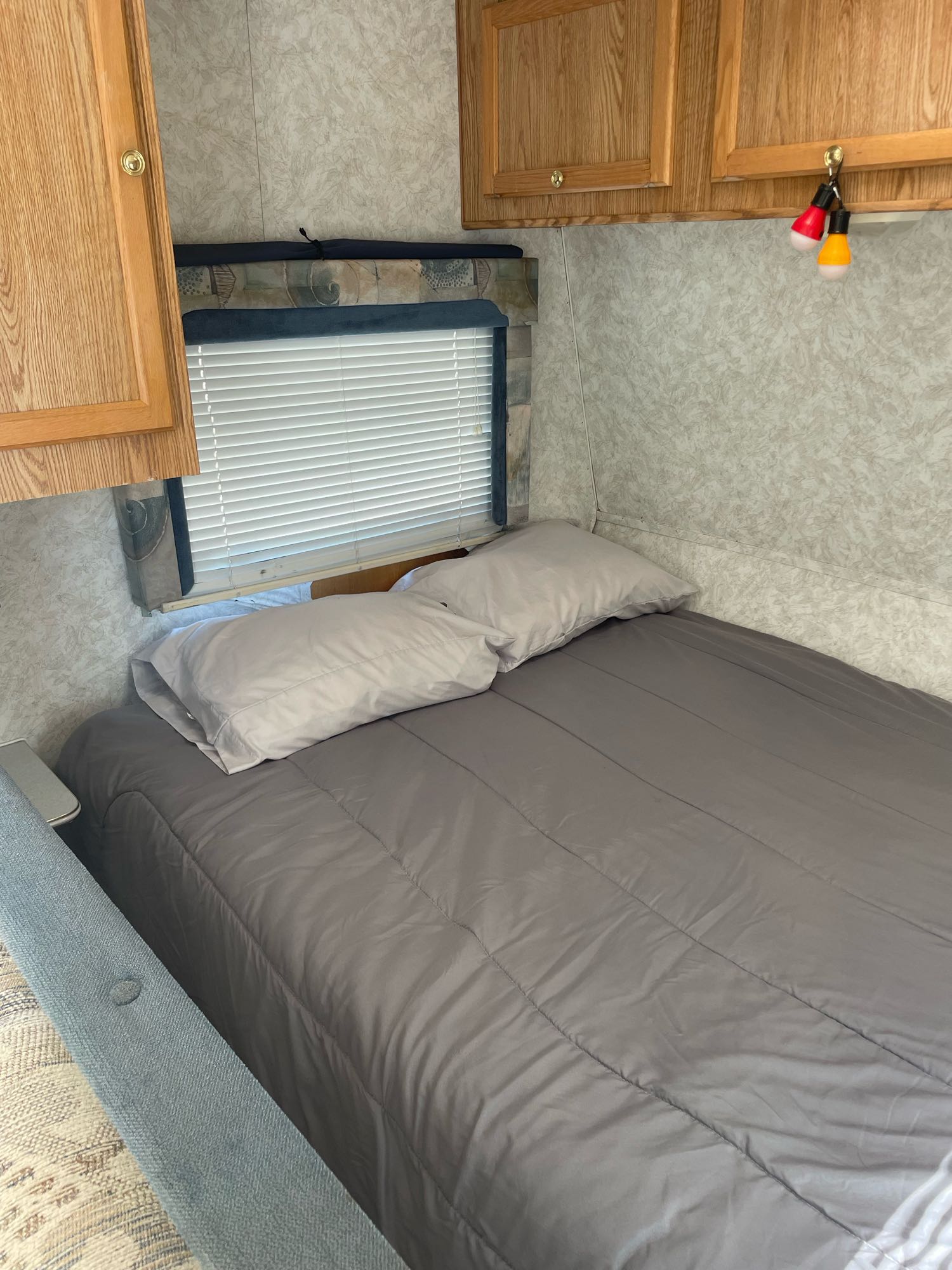Comfortable RV rental bedroom with a grey bed, pillows, wooden cabinets, and a window with blinds.. Thor Wanderer 2001