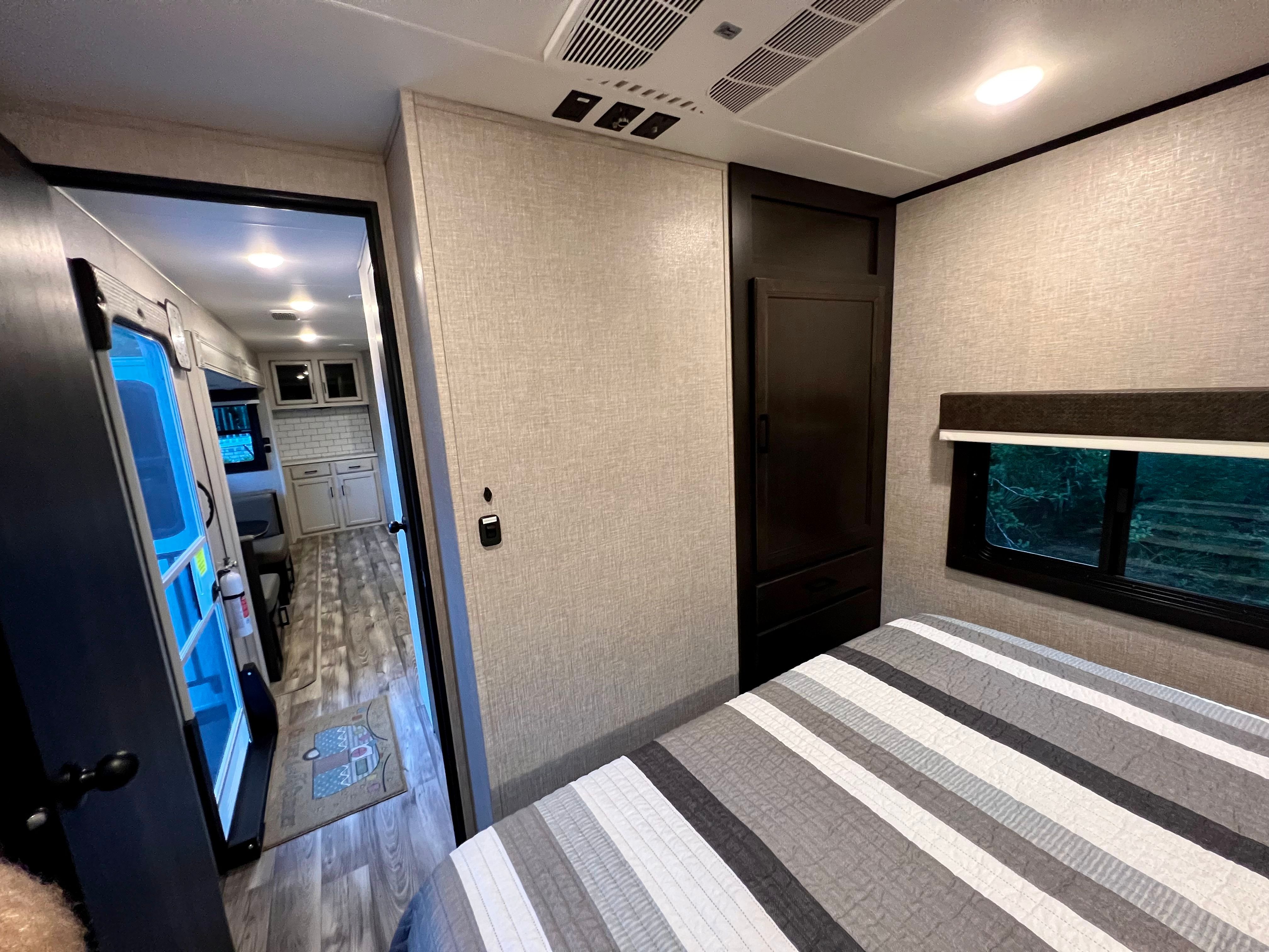 Cozy RV rental interior, showing a bedroom with a striped bed quilt, dark wood closet, and a glimpse of the kitchen area.. Jayco Eagle HT 2022