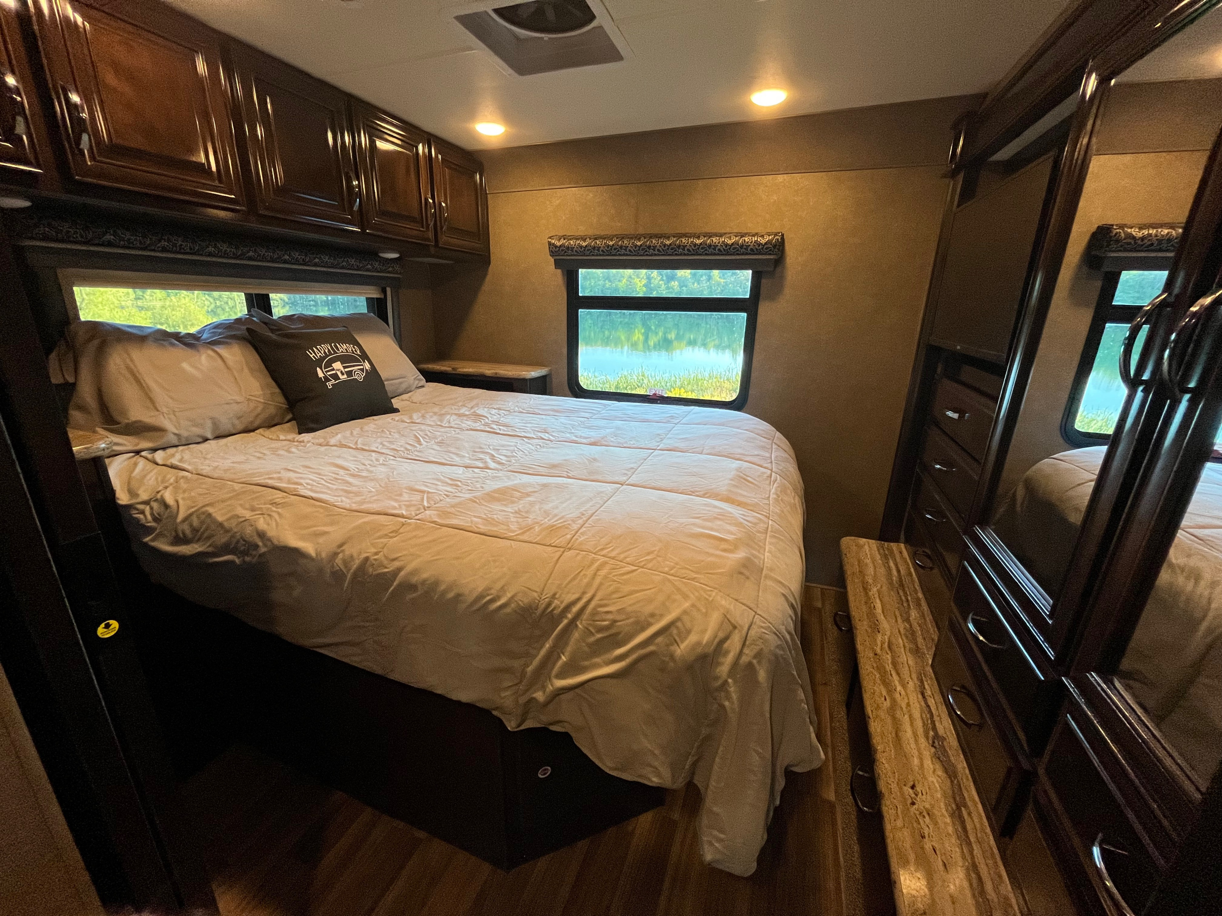 Experience comfort in this RV rental bedroom, featuring a cozy bed, built-in storage, and scenic lake views.. Thor Quantum 2017