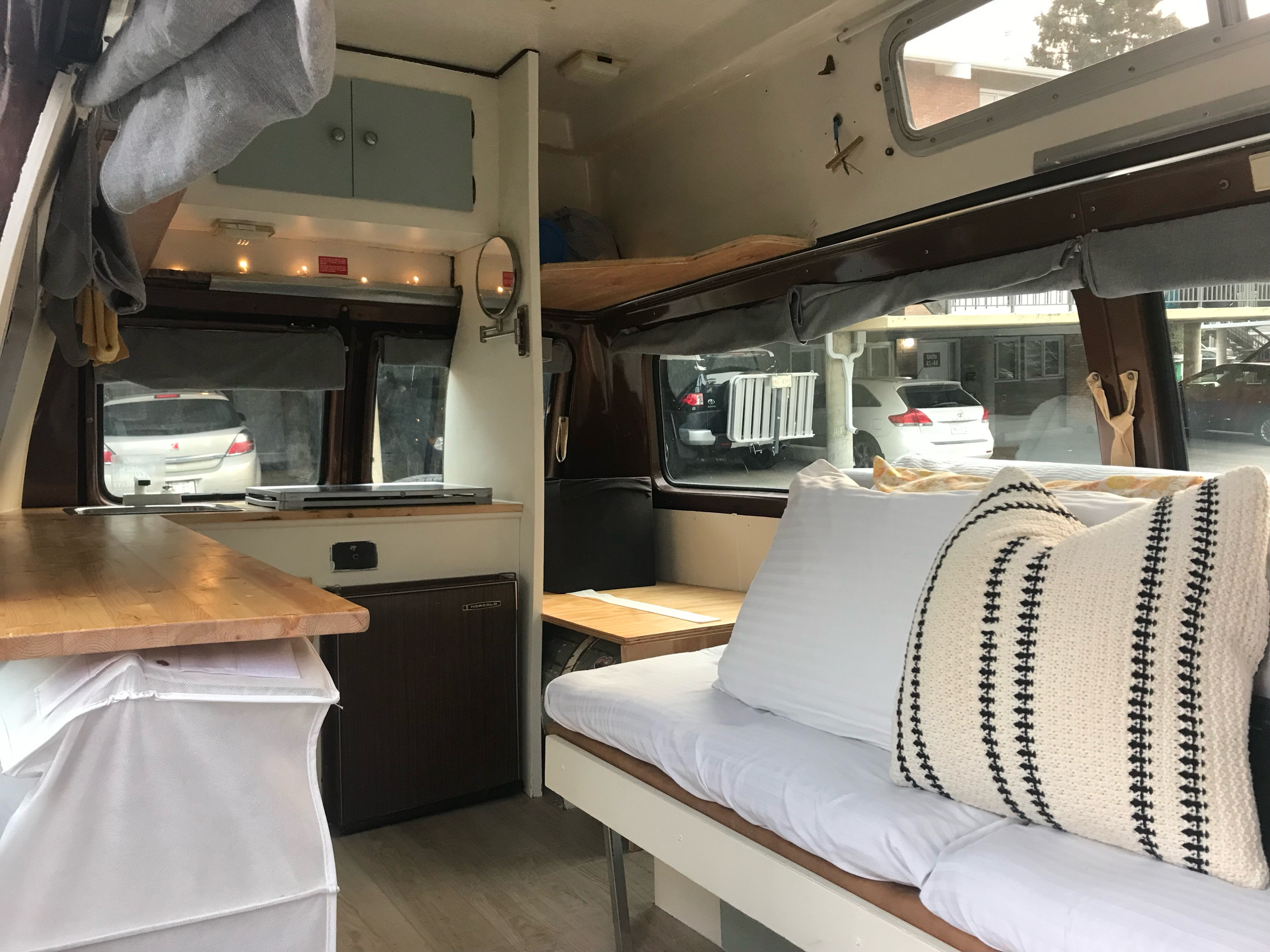 RV rental campervan interior: cozy living space with wooden counter, mini-fridge, and bed with pillows for comfort.. Chevrolet g20 1980