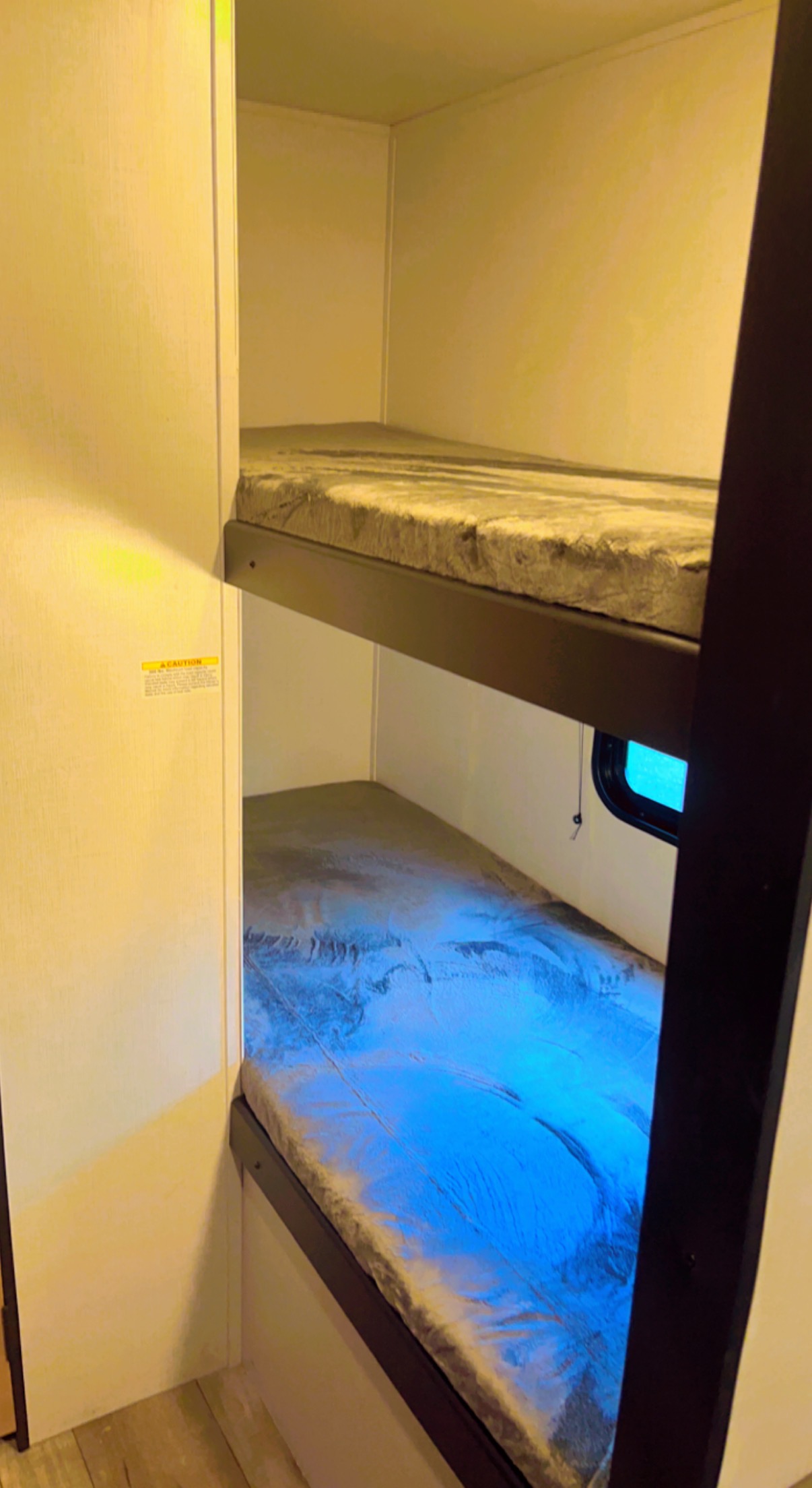 Bunk beds in a compact RV rental, with a bright blue sheet on the lower bed and small window.. Keystone RV Springdale 2022