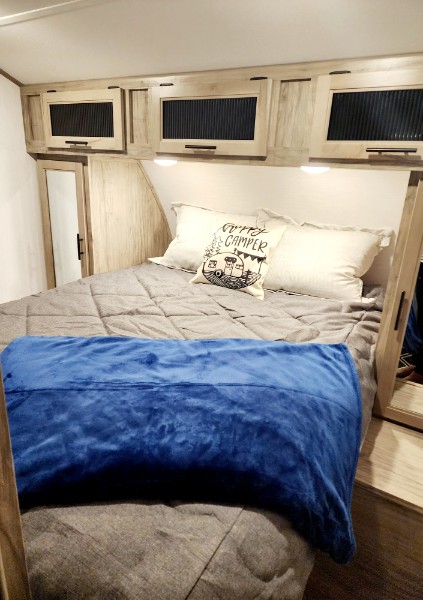 Cozy RV rental bedroom featuring a comfy bed, "Happy Camper" pillow, and overhead storage cabinets.. Forest River Cherokee Alpha Wolf 2022