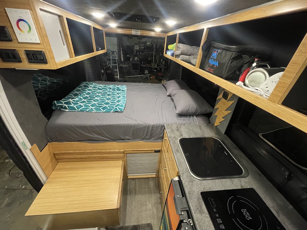 Modern camper van interior for your RV rental adventure: comfy bed, compact kitchen, and smart wood storage.. Ram Promaster 2017