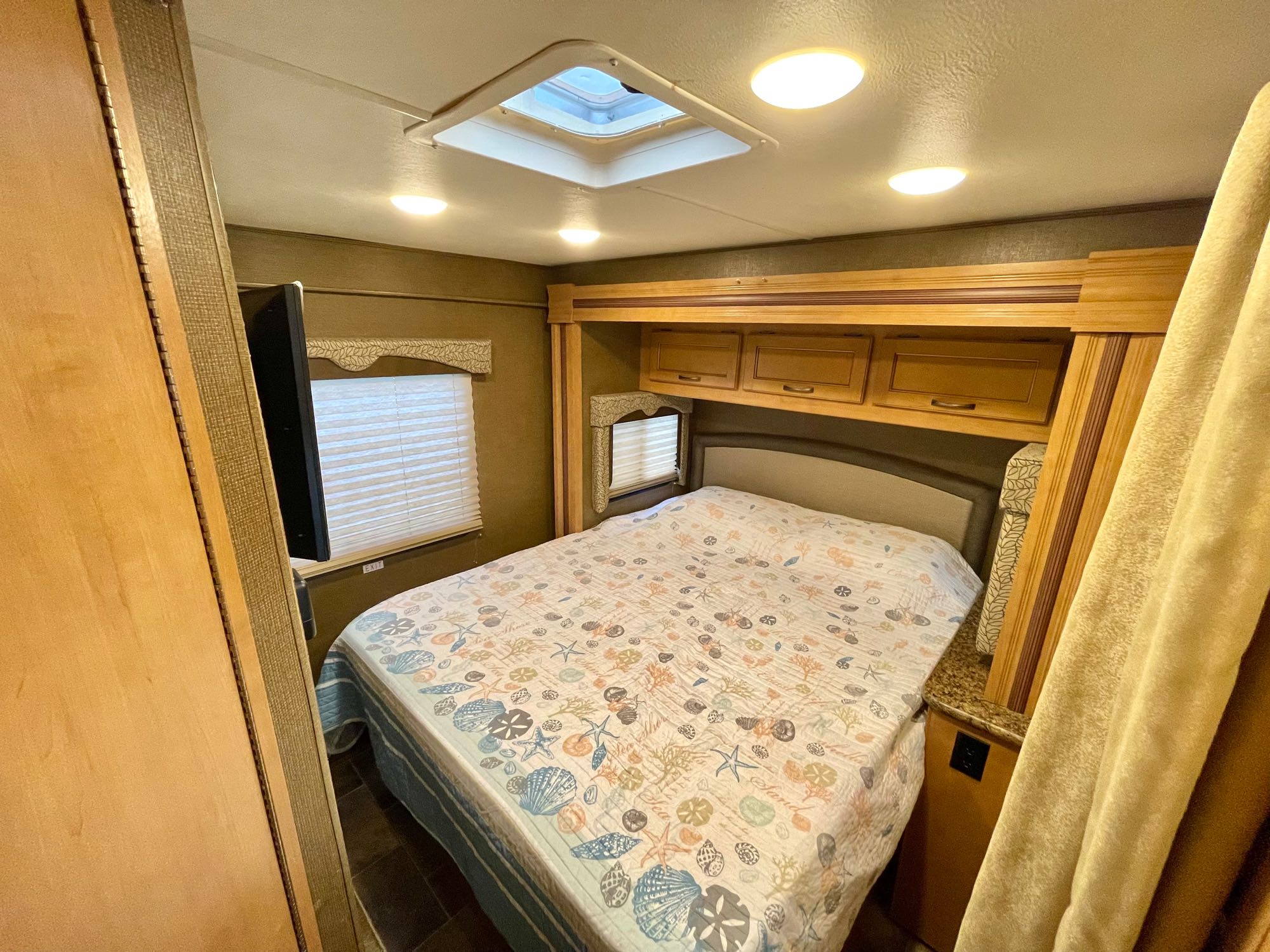 Comfortable RV rental bedroom featuring a patterned bed, overhead storage, skylight, and TV. Perfect for your travels.. Thor Freedom Elite 2017