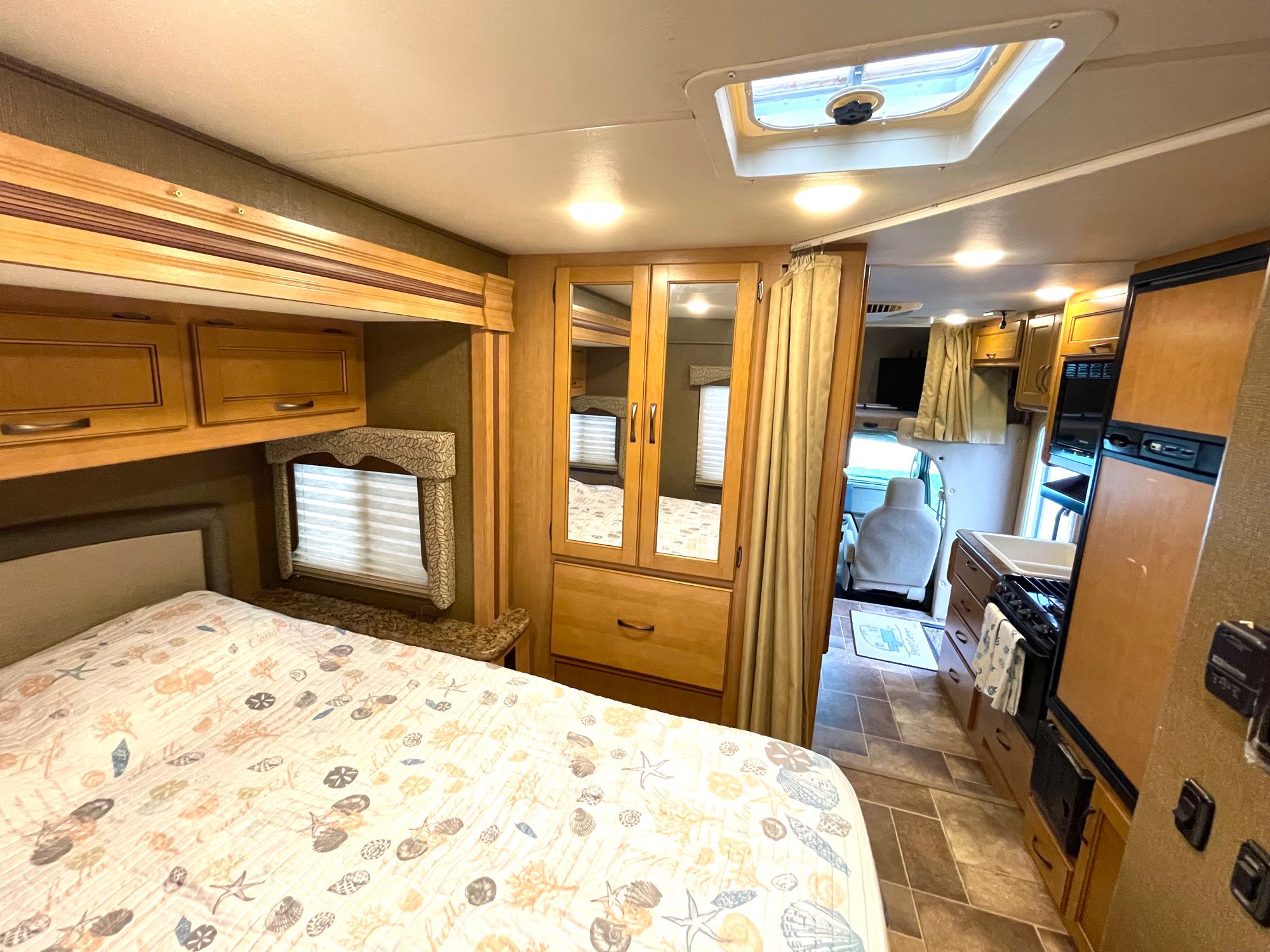Explore this rv rental's interior: comfy bed, wooden cabinetry, mirrored wardrobe, and compact kitchen.. Thor Freedom Elite 2017