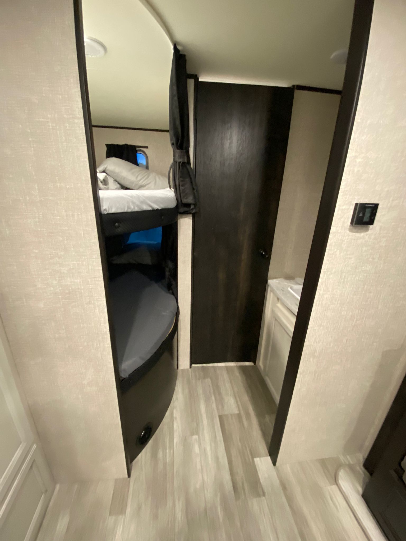 This RV rental features efficient bunk beds, a dark wood bathroom door, and a white sink vanity visible in the compact interior.. Jayco 267 BHS 2022