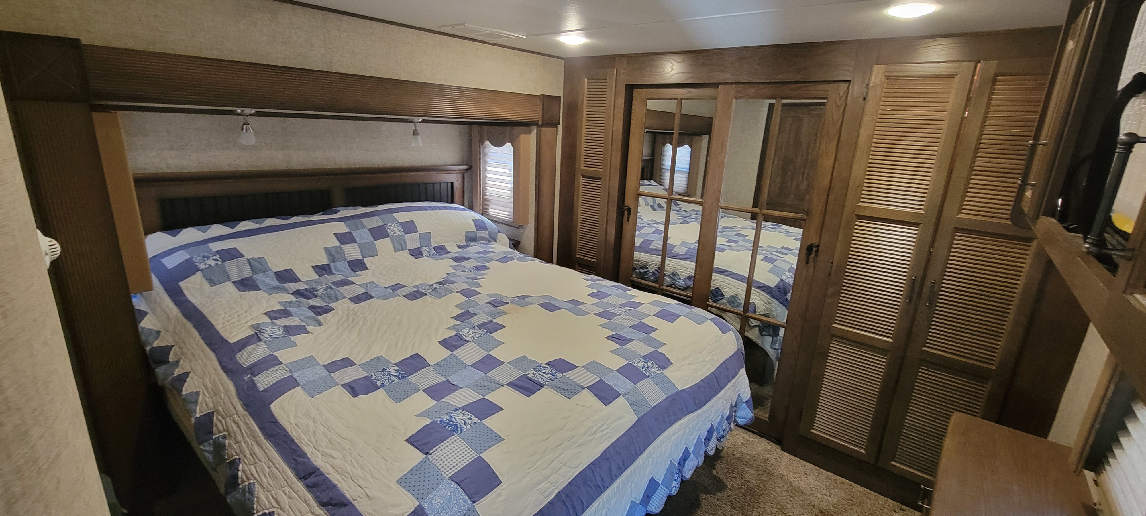 Cozy RV rental bedroom with a blue patterned quilt, wood headboard, and mirrored closet doors reflecting the bed.. Keystone RV Alpine 2015