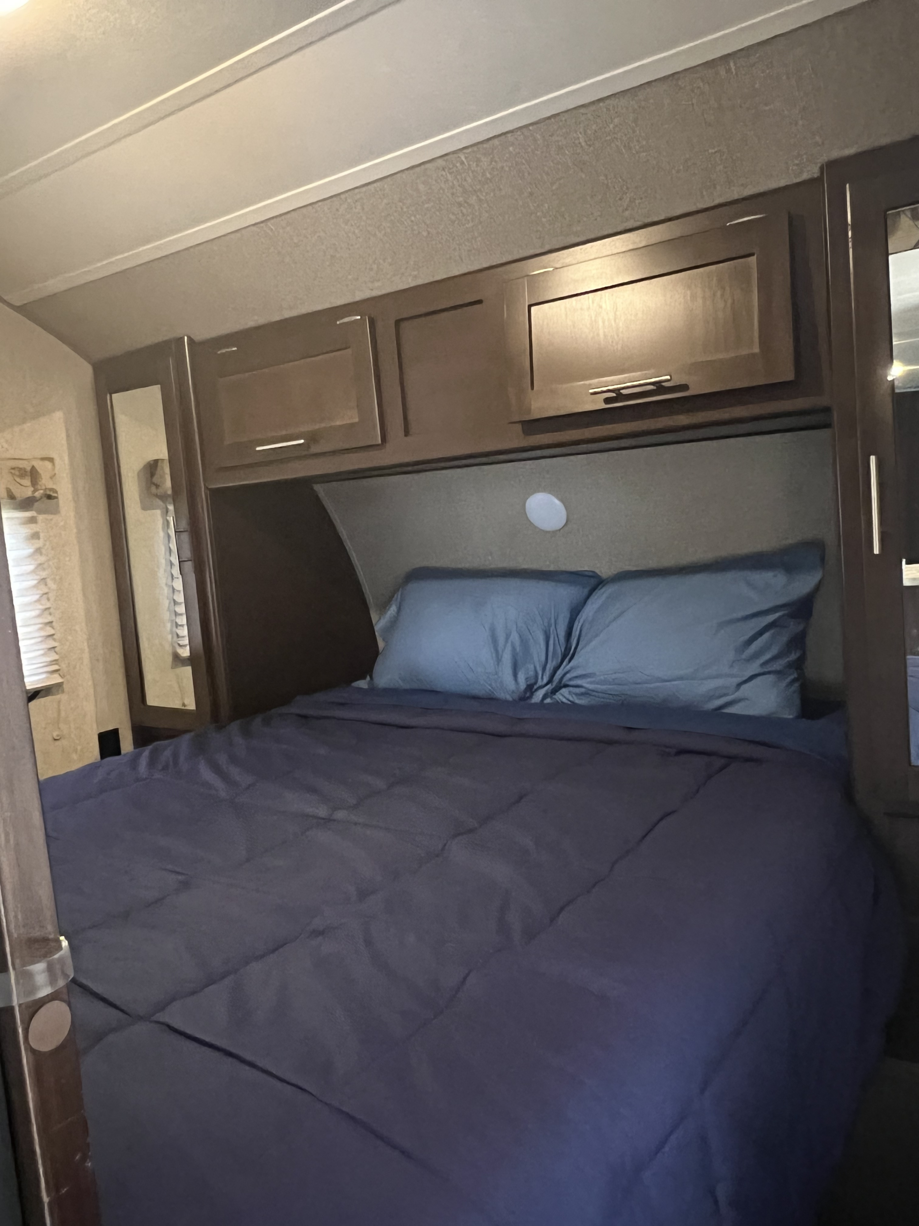 Cozy RV rental bedroom featuring a large bed with dark blue bedding, overhead cabinets, and mirrored wardrobes.. Forest River Cherokee Grey Wolf 2016