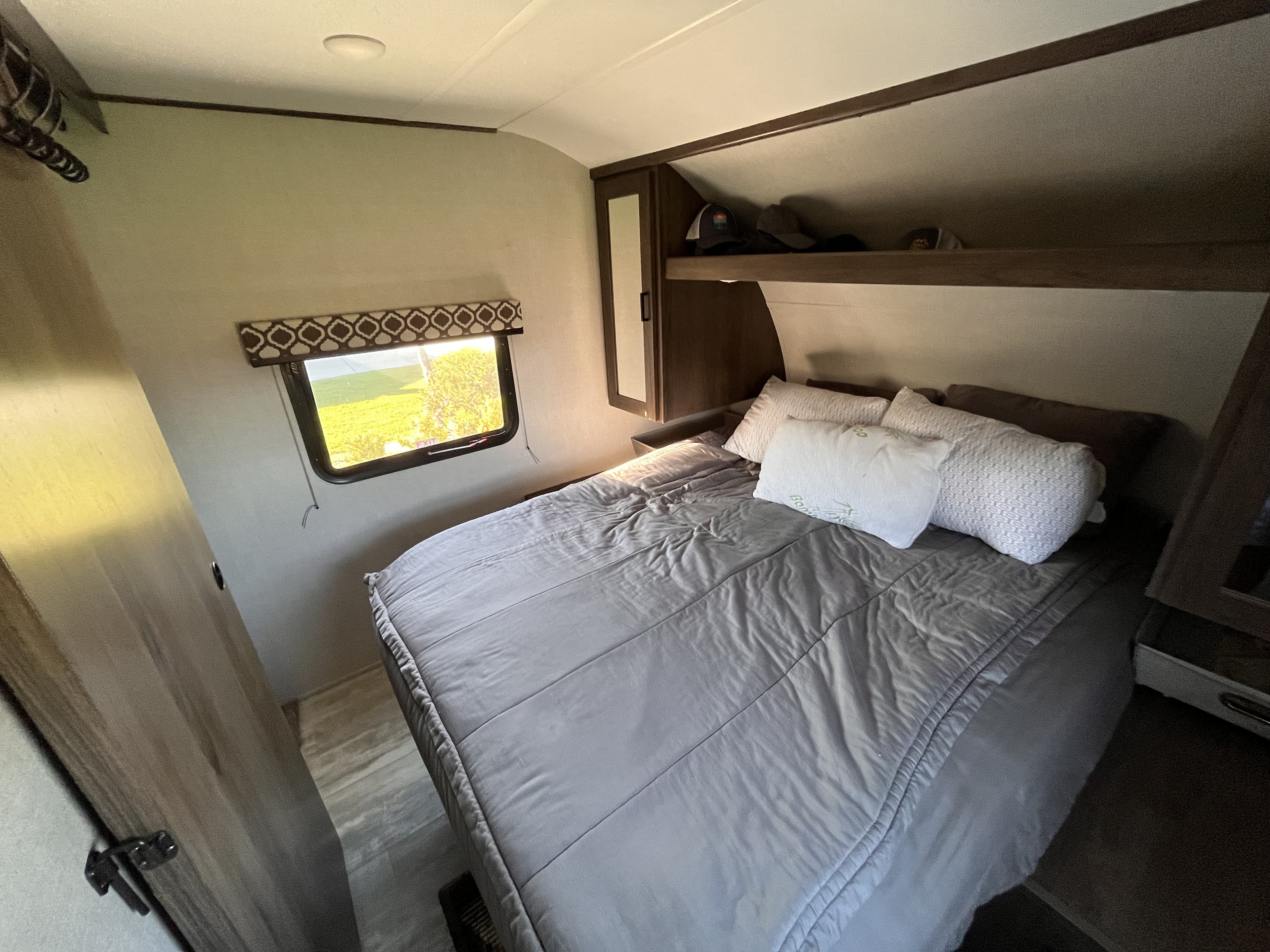 Bright RV rental bedroom features a comfy bed, window with nature views, and convenient overhead storage.. Forest River Tracer 2021