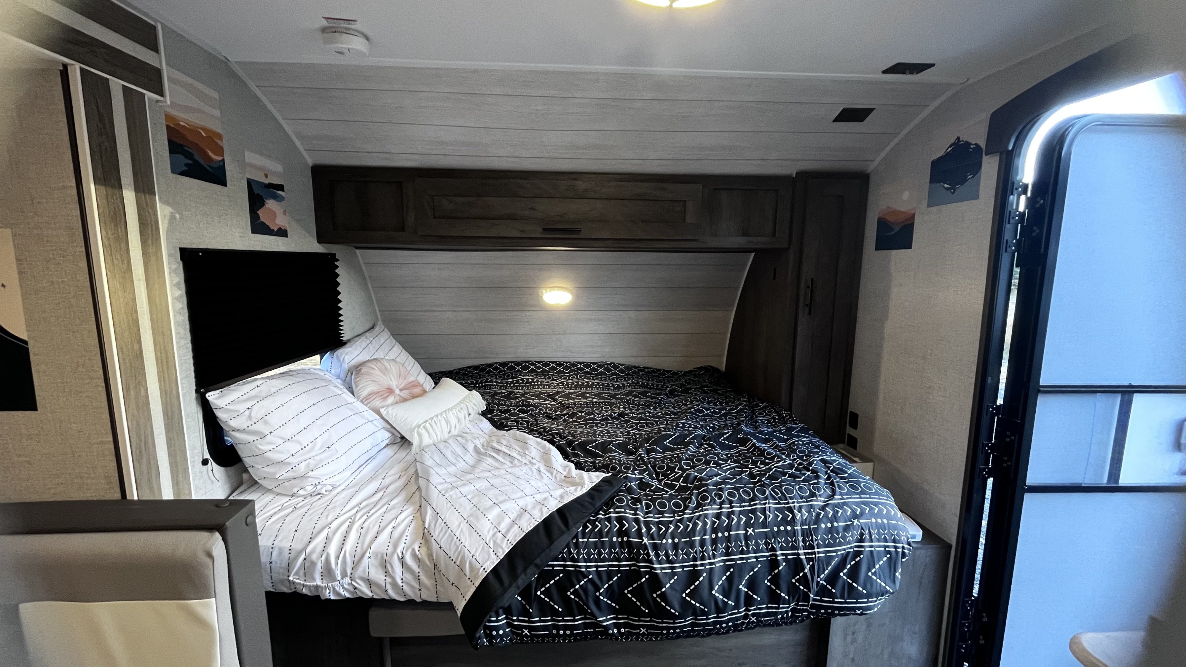 Cozy RV rental bedroom featuring a full bed with black & white patterned bedding, pillows, and wall art. Ideal compact interior.. Forest River Wildwood FSX 2021