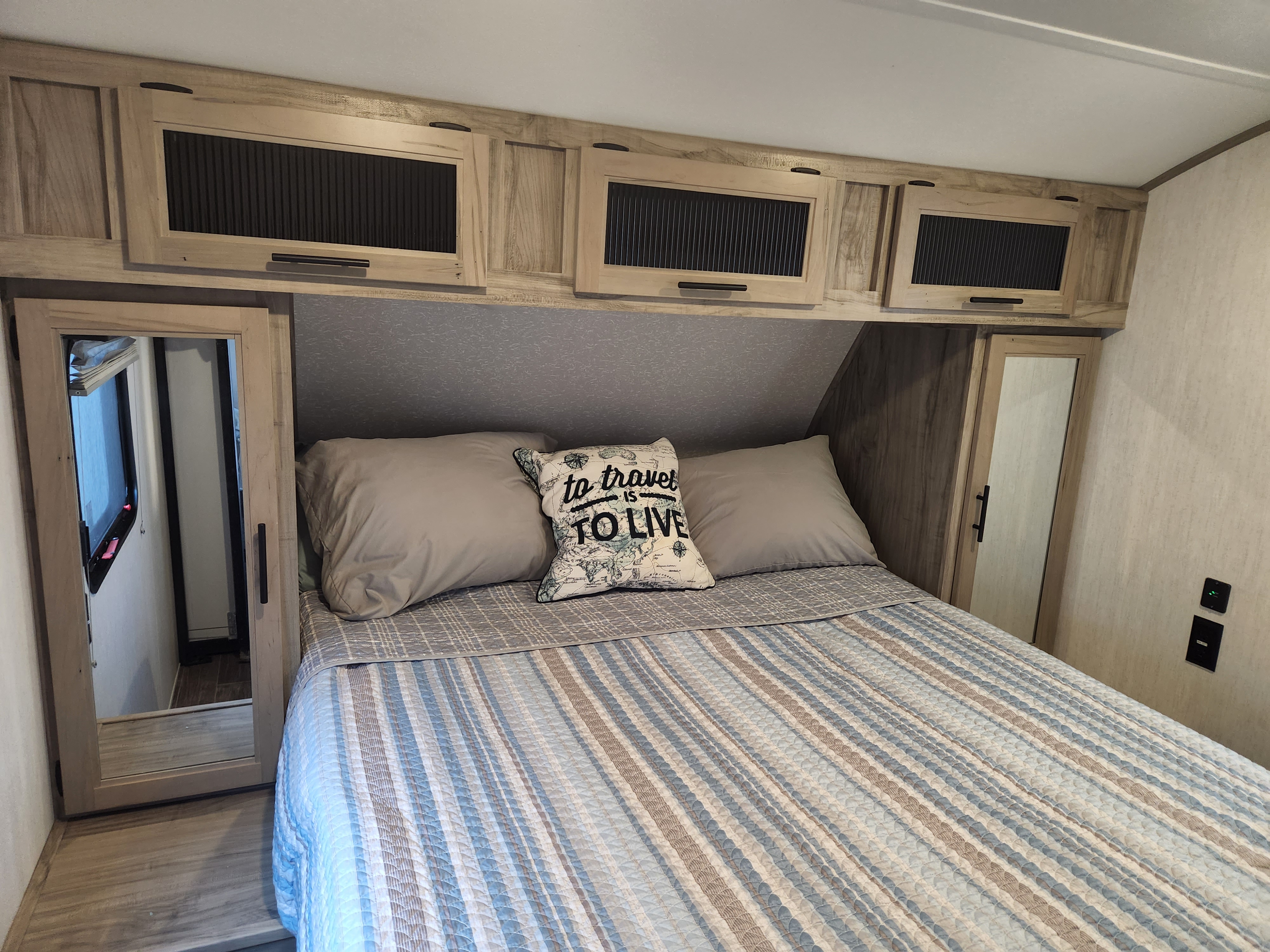 Explore this cozy RV rental bedroom. It features a comfy bed, functional overhead storage, and mirrored wardrobe doors.. Forest River Cherokee Alpha Wolf 2022