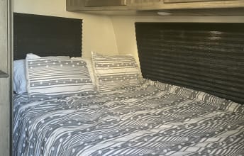 Inside an RV rental: a cozy bedroom with a bed, grey and white striped bedding, and pillows, offering comfortable accommodations.. Coachmen Apex Nano 2021