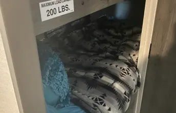 Inside an RV rental, a cozy bunk bed with patterned bedding and a sign showing 200 lbs max load capacity.. Coachmen Apex Nano 2021