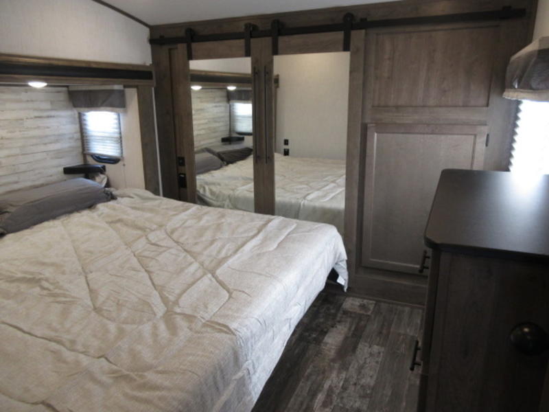 Inside a modern RV rental bedroom featuring a comfy bed, wood-paneled walls, and mirrored closet doors.. Forest River Cherokee Sabre 2022