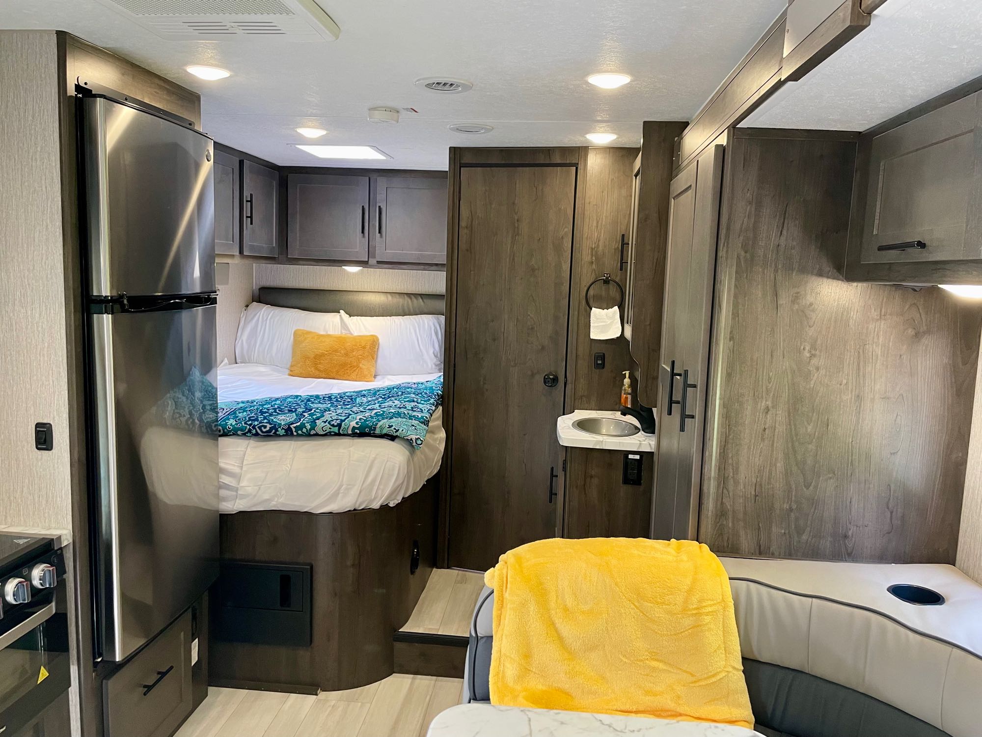 Inside this RV rental, discover a cozy bed, compact stainless steel refrigerator, kitchen, and a small sink area.. Forest River Coachmen Prism Elite 2023