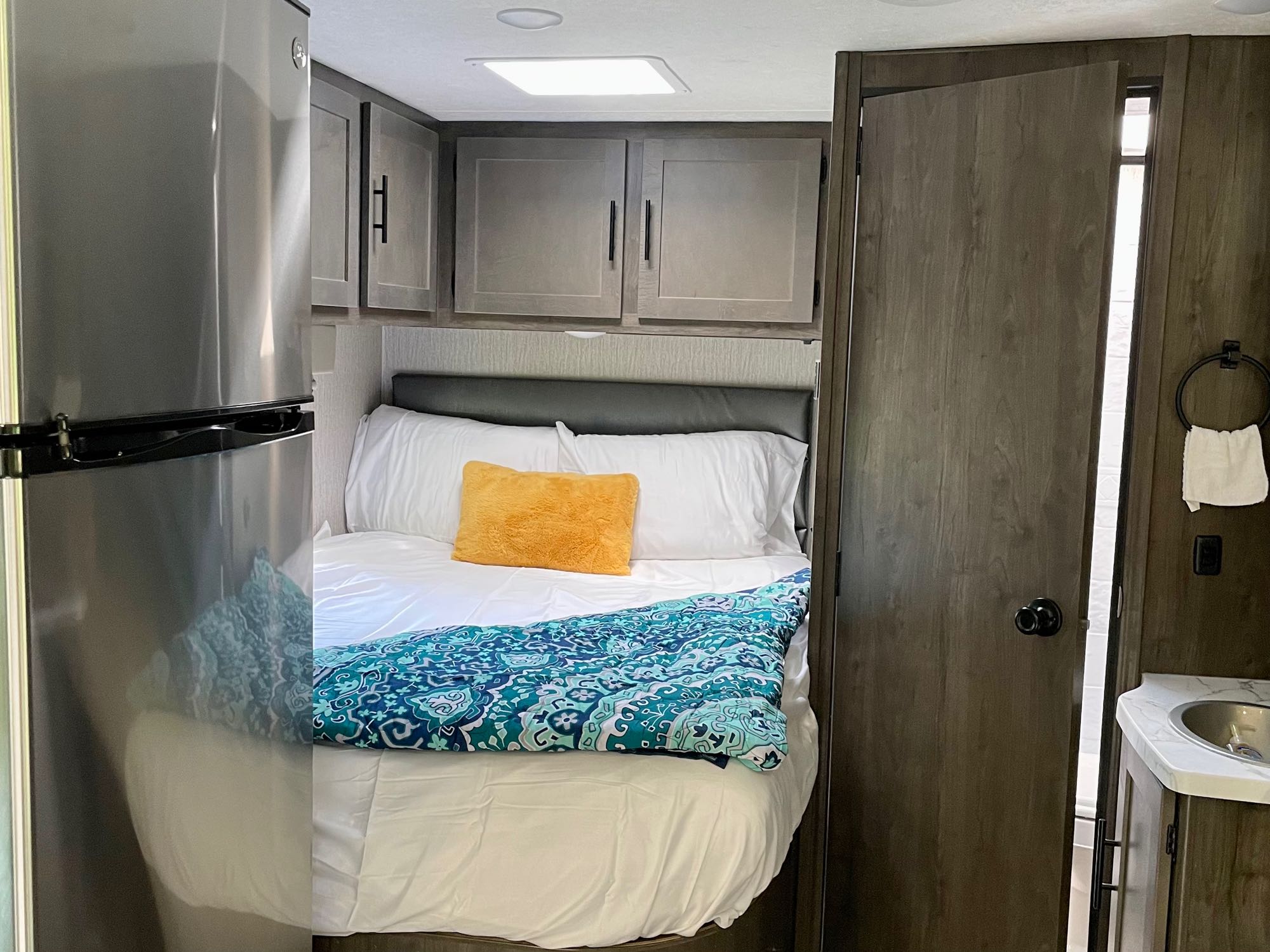 Comfortable RV rental interior: bedroom with bed, overhead storage, & partial kitchen/bath view for your next adventure.. Forest River Coachmen Prism Elite 2023