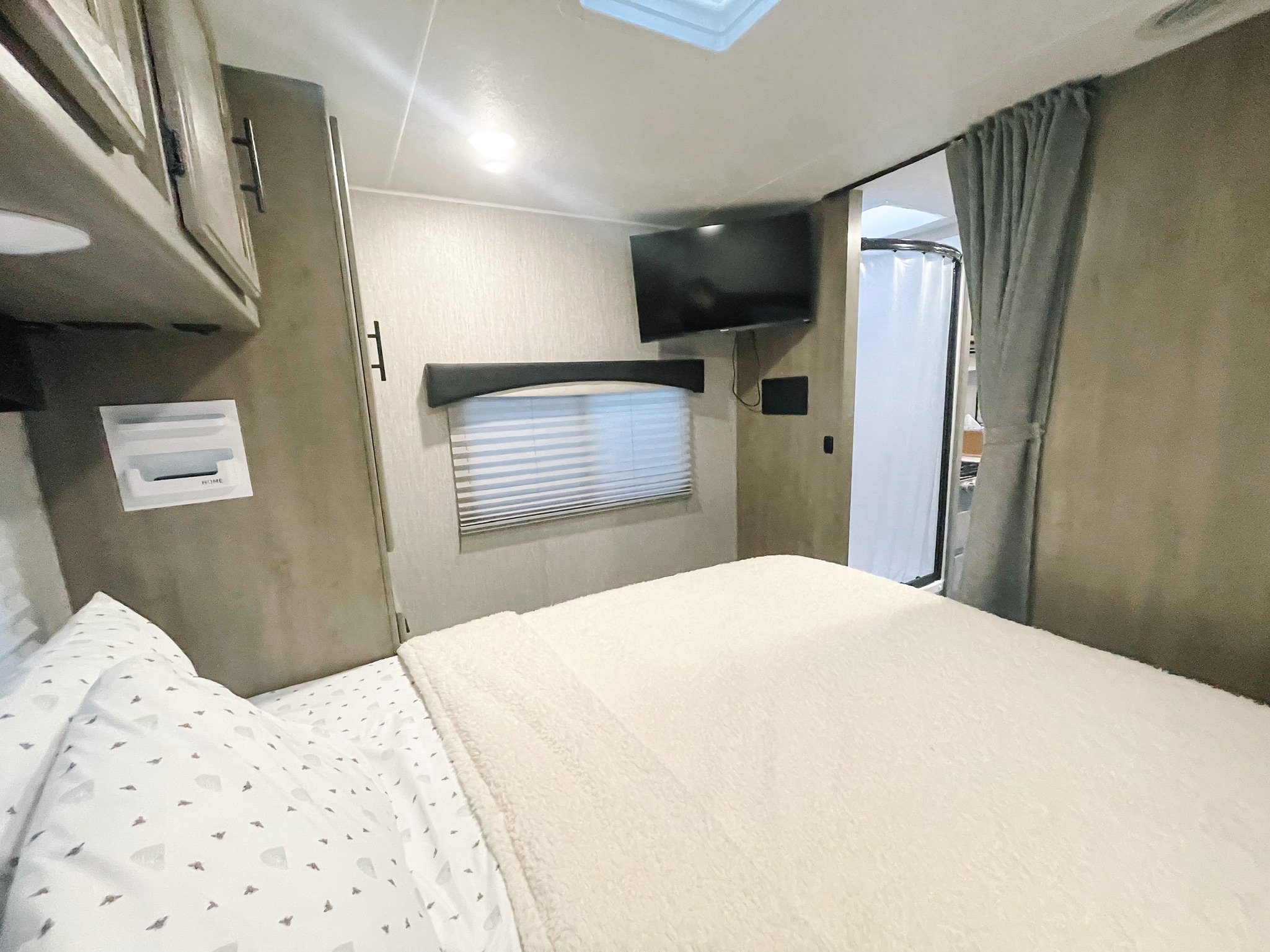 Comfortable RV rental bedroom featuring a cozy bed, wall-mounted TV, window, and a visible attached bathroom area.. COACHMEN FREELANDER 2021