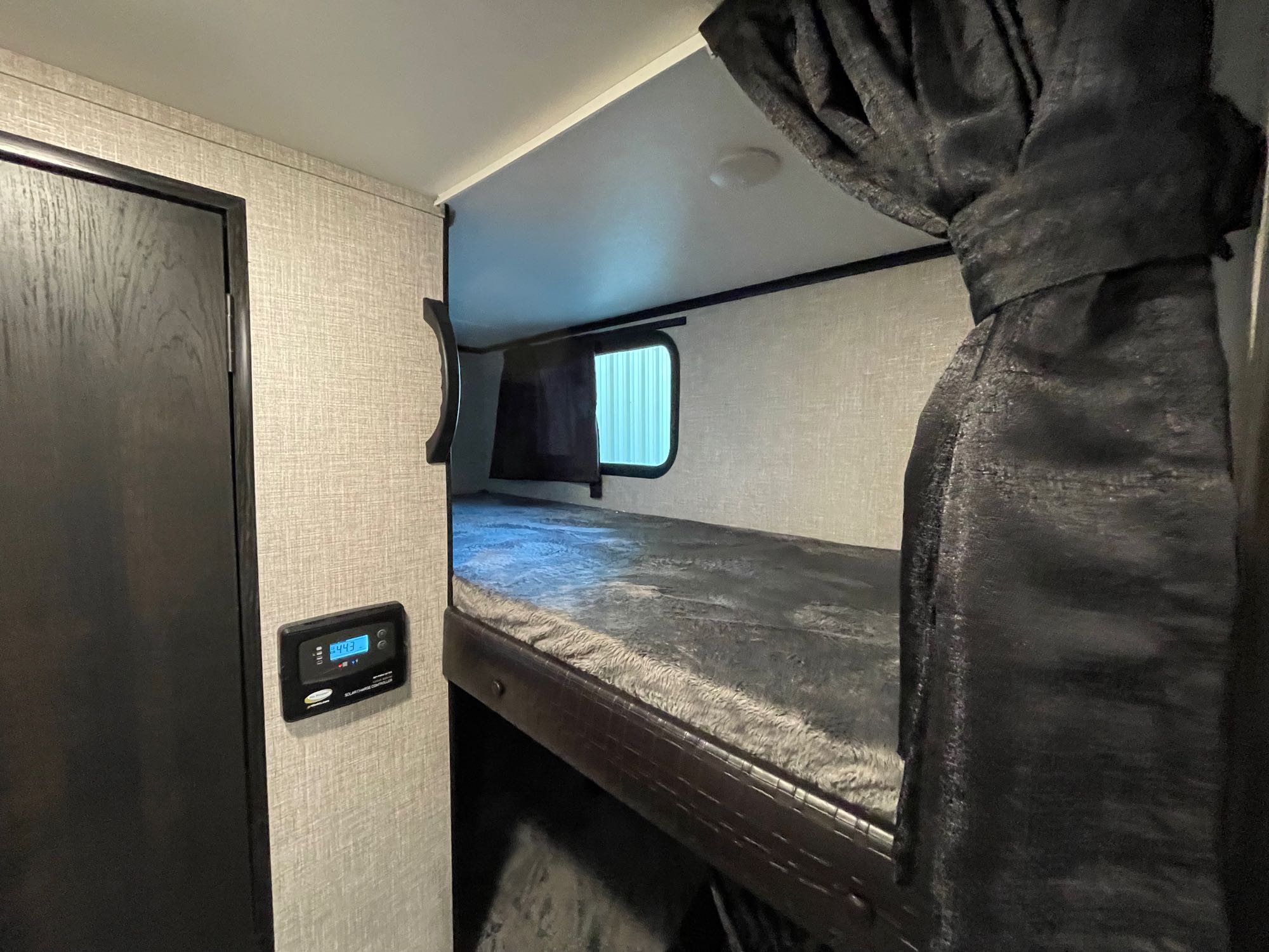 Cozy RV rental bunk bed area with privacy curtain, window, and a solar charge controller on the wall.. Jayco Jay Feather 2022