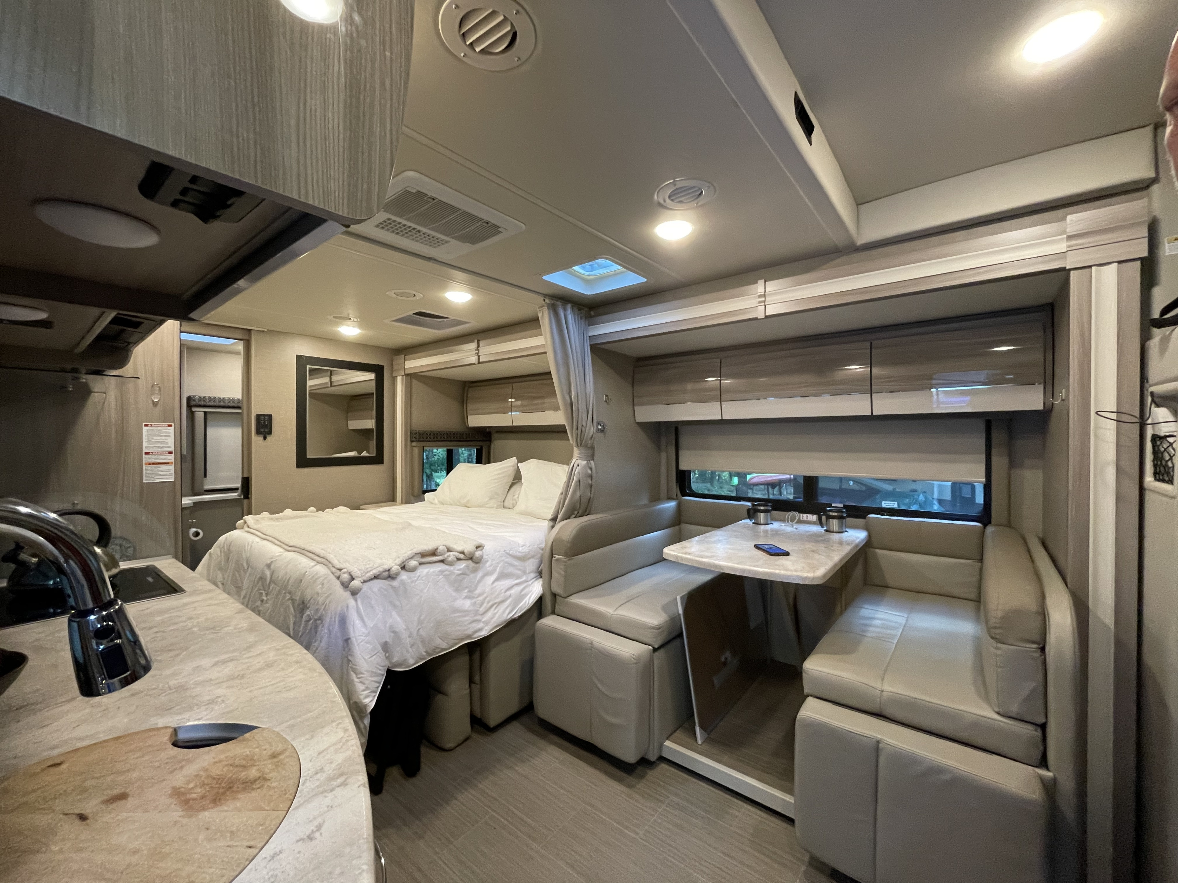 Modern rv rental interior with a comfortable bed, functional dinette, and compact kitchen area for travelers.. Thor Tiburon 2020