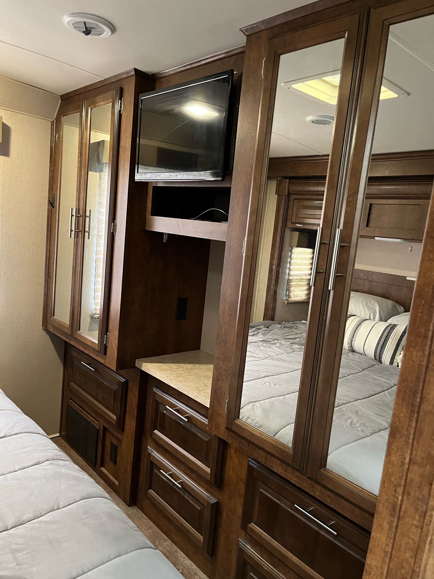 Cozy RV rental bedroom featuring dark wood cabinetry, a comfortable bed, and mirrored closet doors. Ideal for travel.. Forest River FR3 30DS 2015