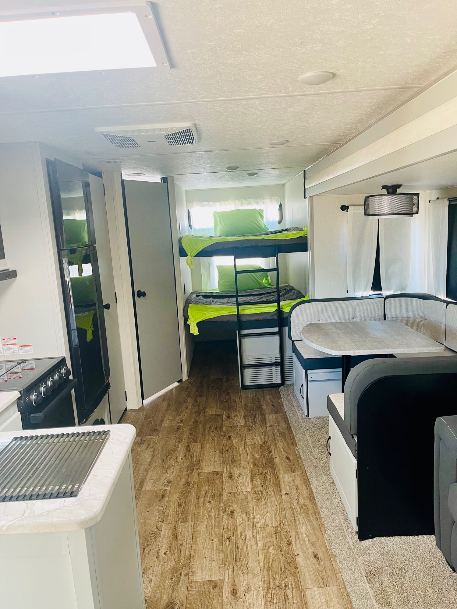 RV rental interior: bunk beds with lime green bedding, dining booth, and kitchen. Features wood-look floor & bright lighting.. Forest River Vibe 2022