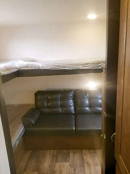 RV rental interior with a top bunk bed (covered) and a dark, tufted sofa below, on a wood-look floor.. Forest River Salem Cruise Lite 2017