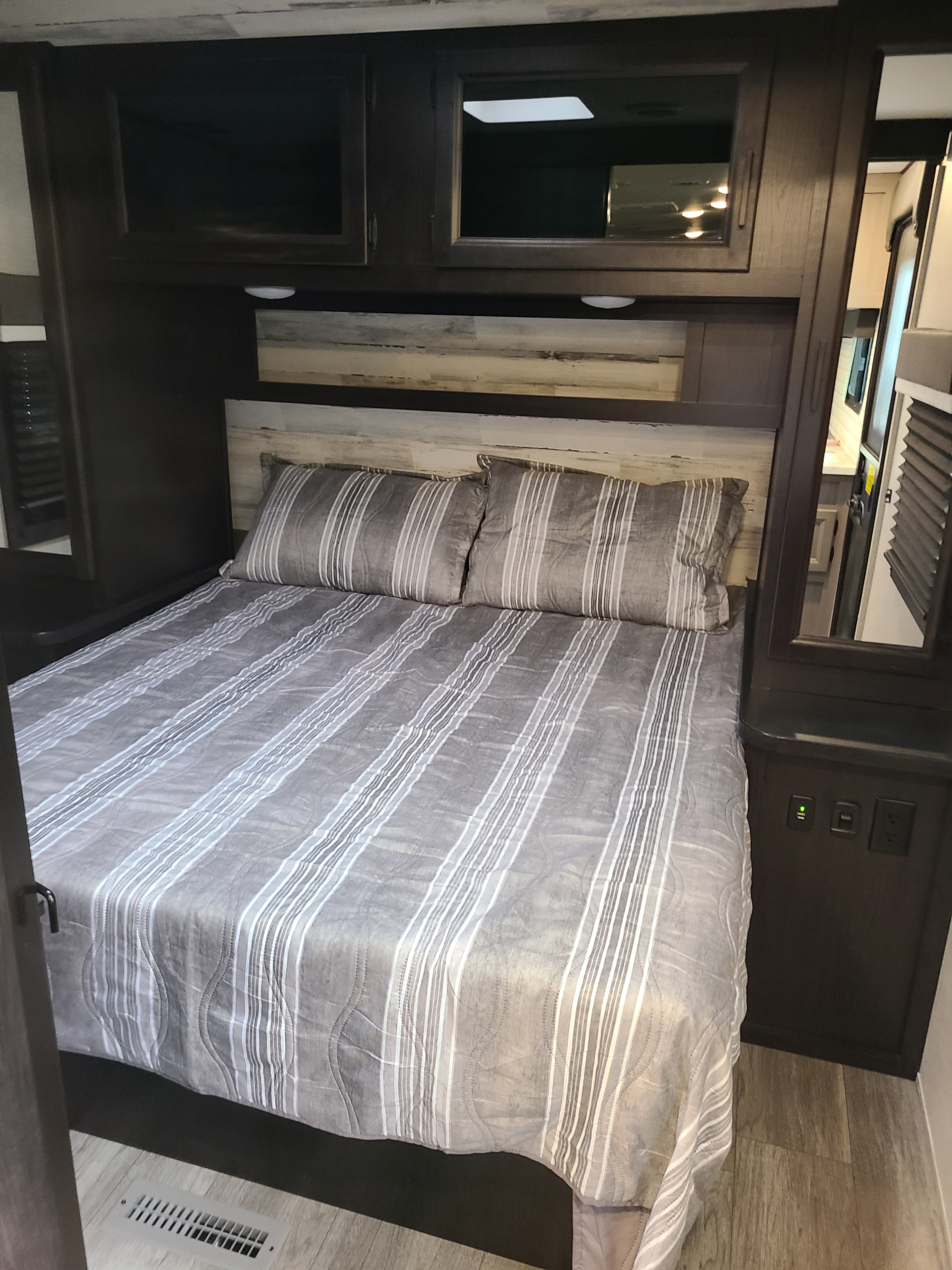 RV rental bedroom featuring a comfy striped bed, overhead storage, and bedside outlets, ideal for a relaxing trip.. Jayco Jay Feather 2022