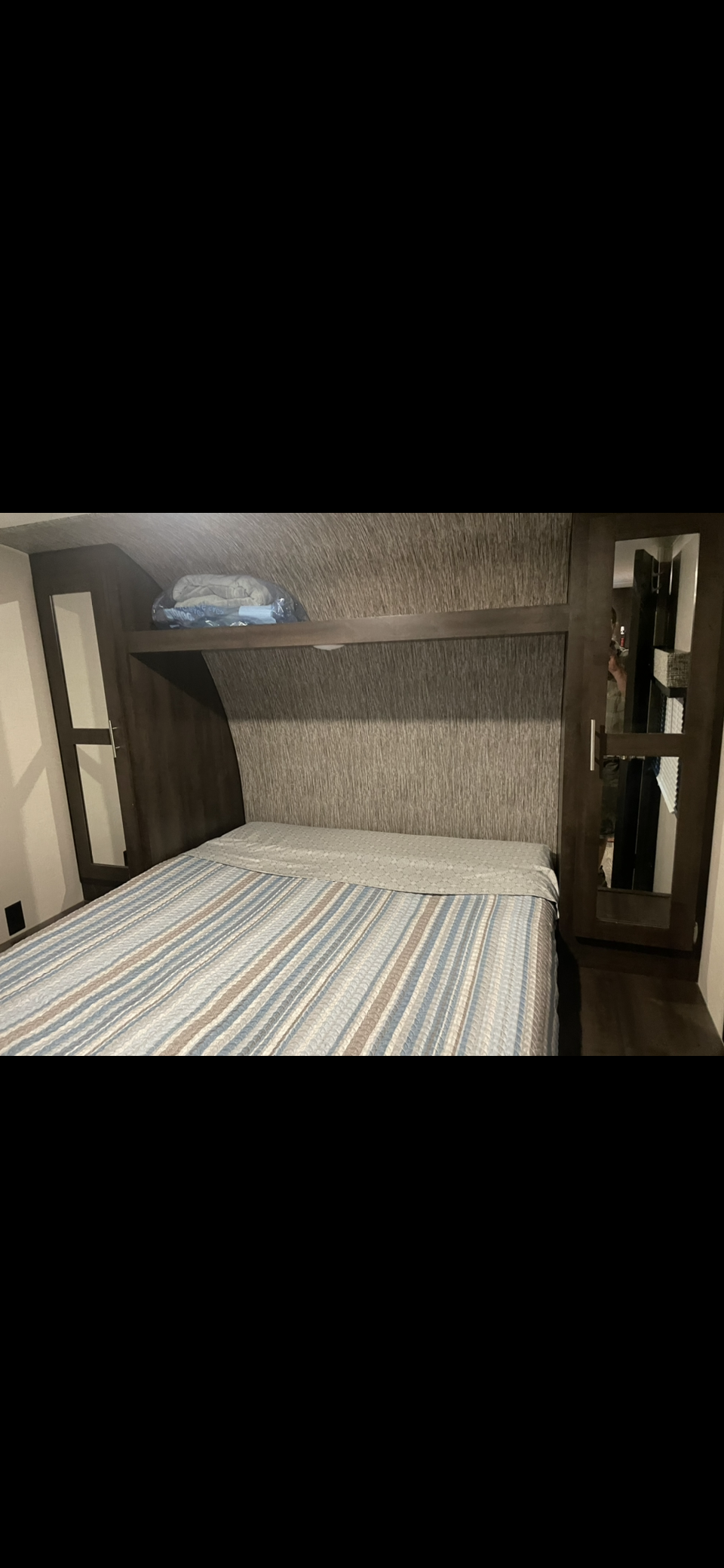 This RV rental bedroom features a blue striped bed, an overhead shelf, and a mirrored closet.. KZ Sportsmen 291RKLE 2019