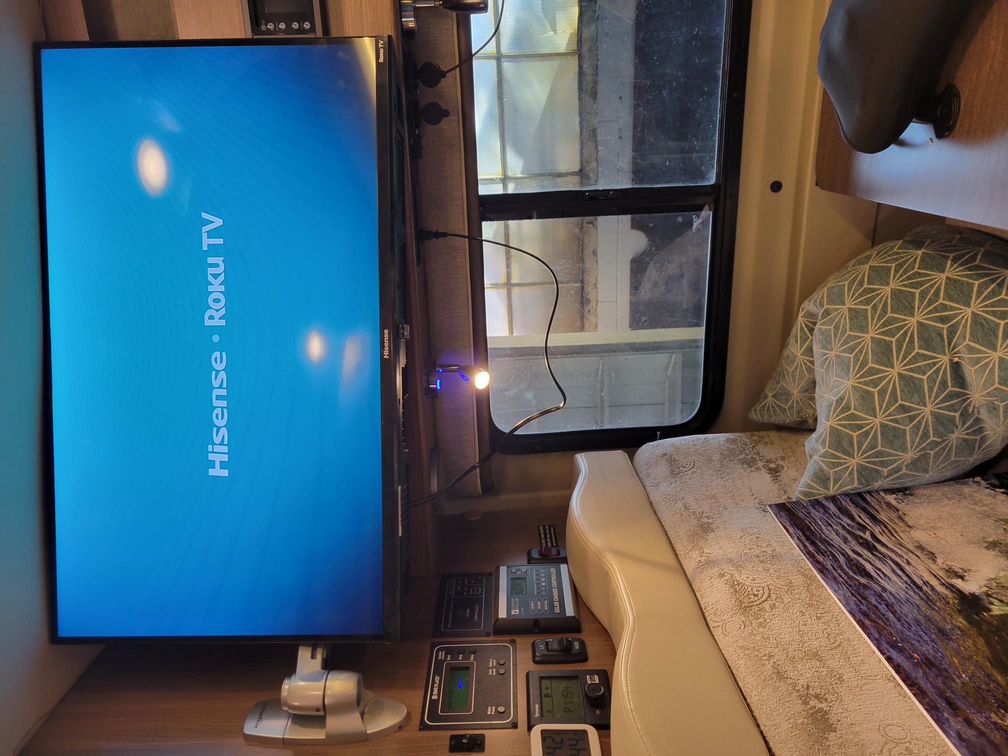 RV rental interior featuring a Hisense Roku TV display, solar charge controller, and cozy bench seating.. Winnebago Travato 2018