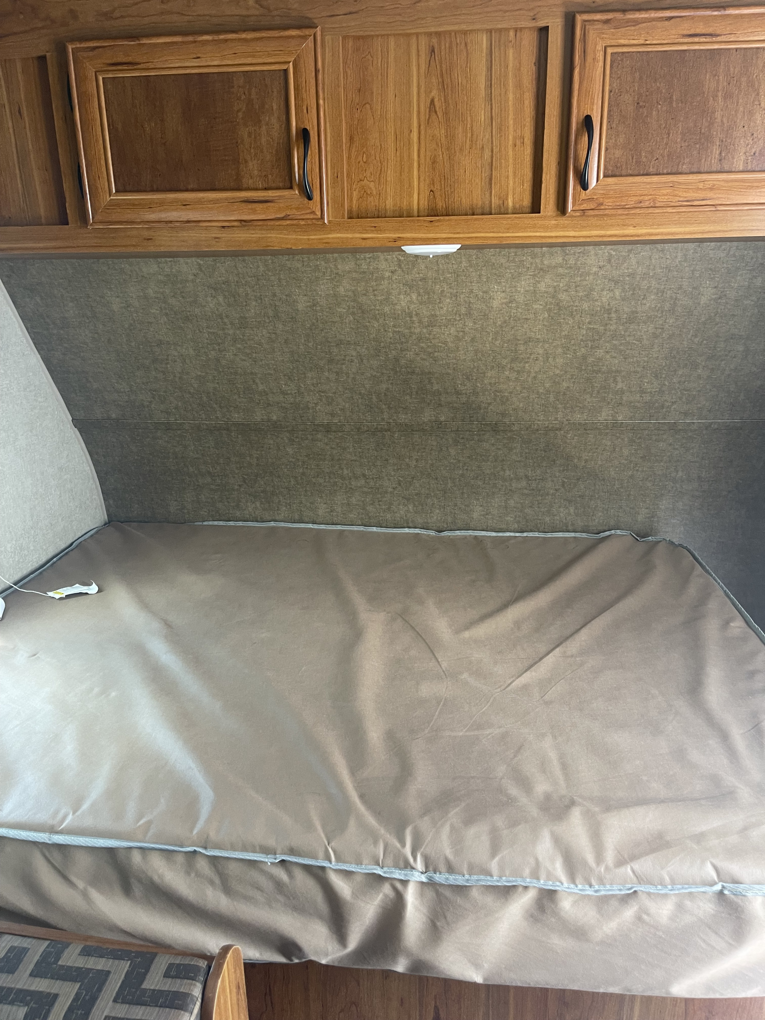 Interior of an RV rental bedroom featuring a tan-covered bed, padded headboard, and functional wood overhead cabinets.. Starcraft Ar-One 2016