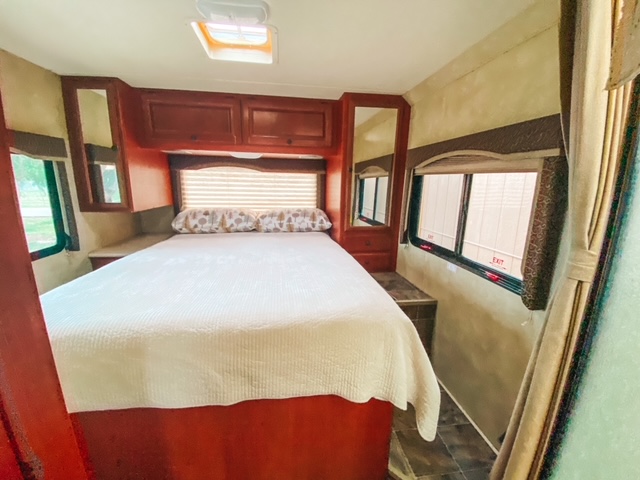 Comfortable RV rental bedroom interior featuring a spacious bed, overhead cabinets, side tables, and windows for a cozy travel space.. Thor Freedom Elite 2012