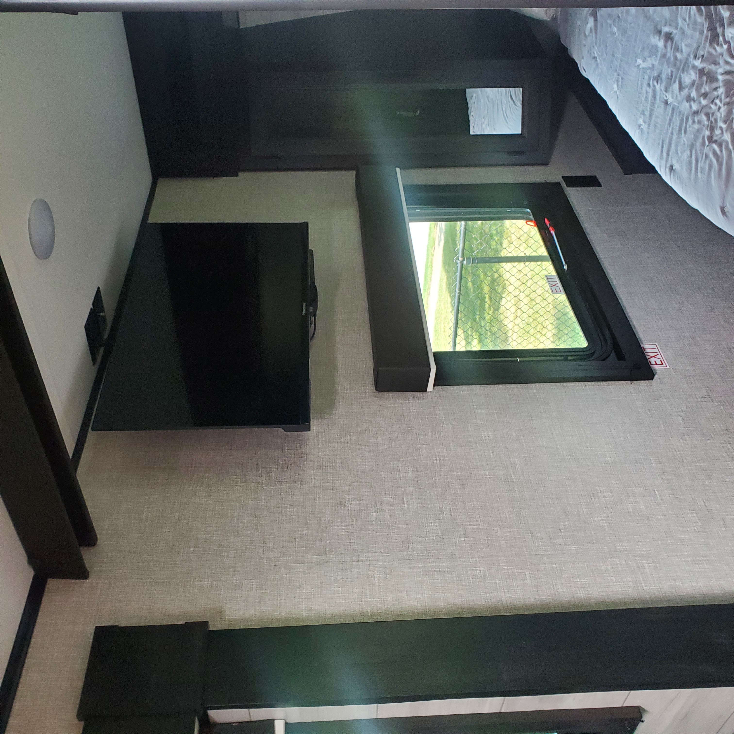 Cozy RV rental interior with a wall-mounted TV, window overlooking greenery, and a comfortable bed. Ideal compact living space.. Jayco Jay Flight 2022