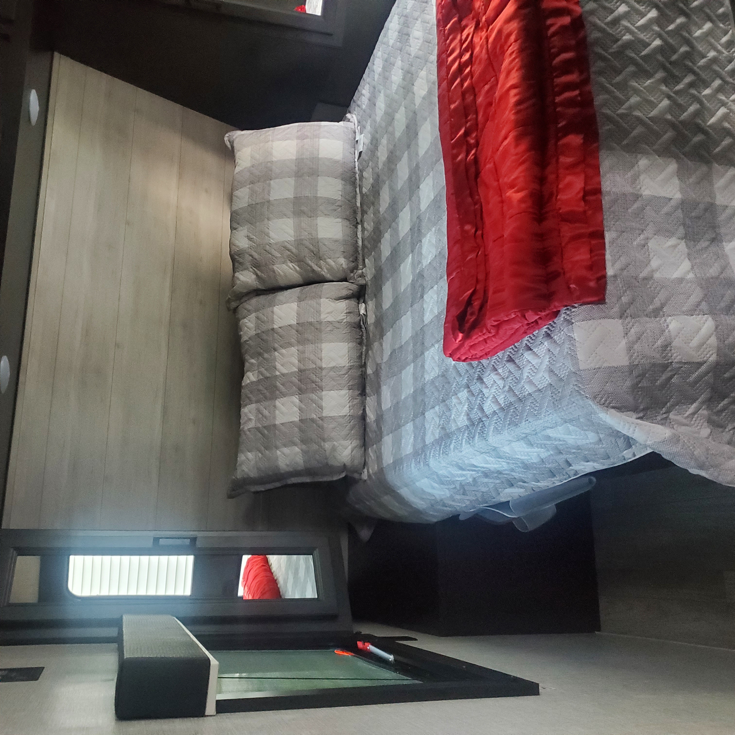 Step inside this inviting RV rental bedroom featuring a comfy bed with gray plaid bedding, a vibrant red blanket, and light wood walls.. Jayco Jay Flight 2022