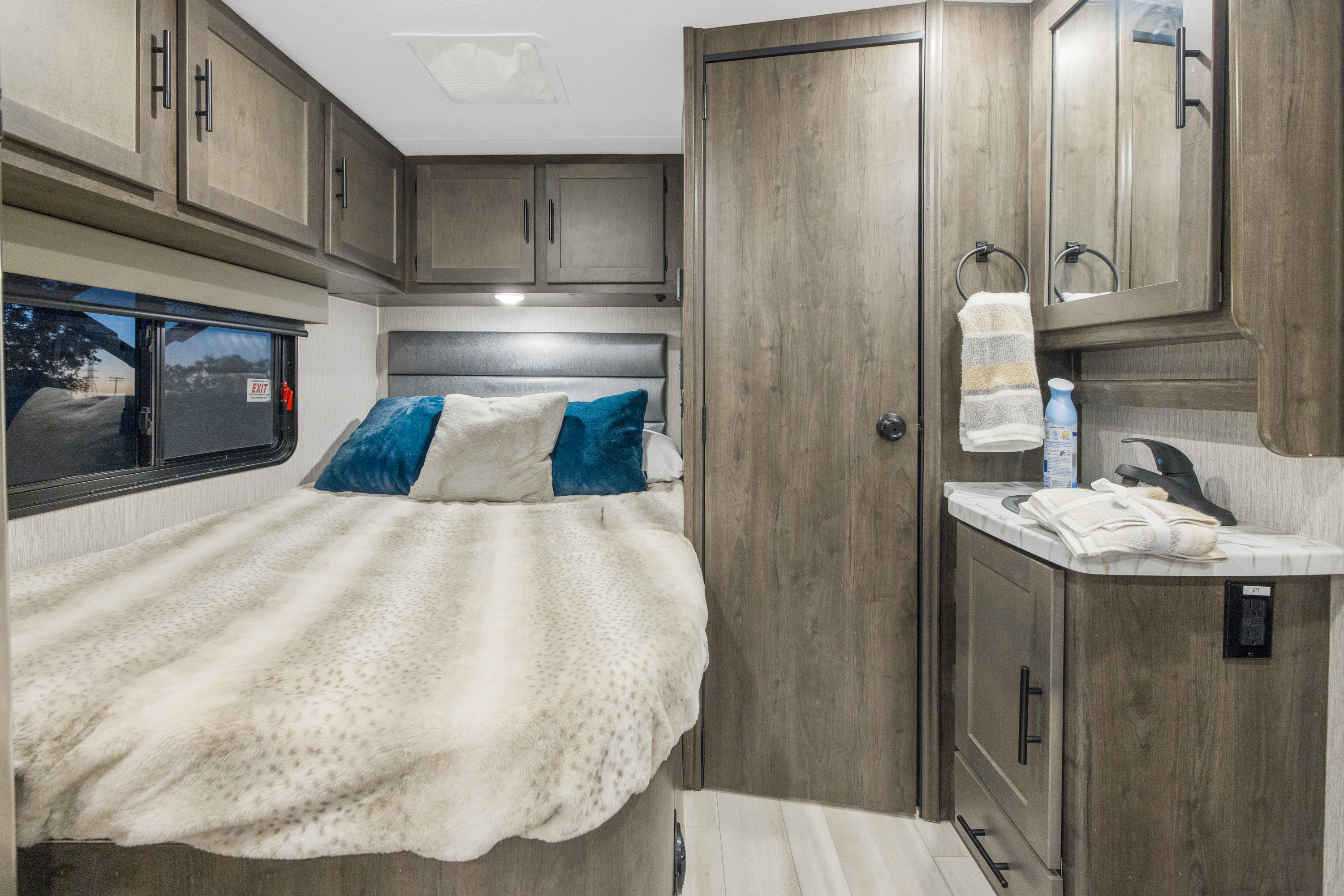 Cozy RV rental bedroom with comfortable bed, overhead cabinets, and a compact vanity area with mirror.. Coachmen Prism 2023