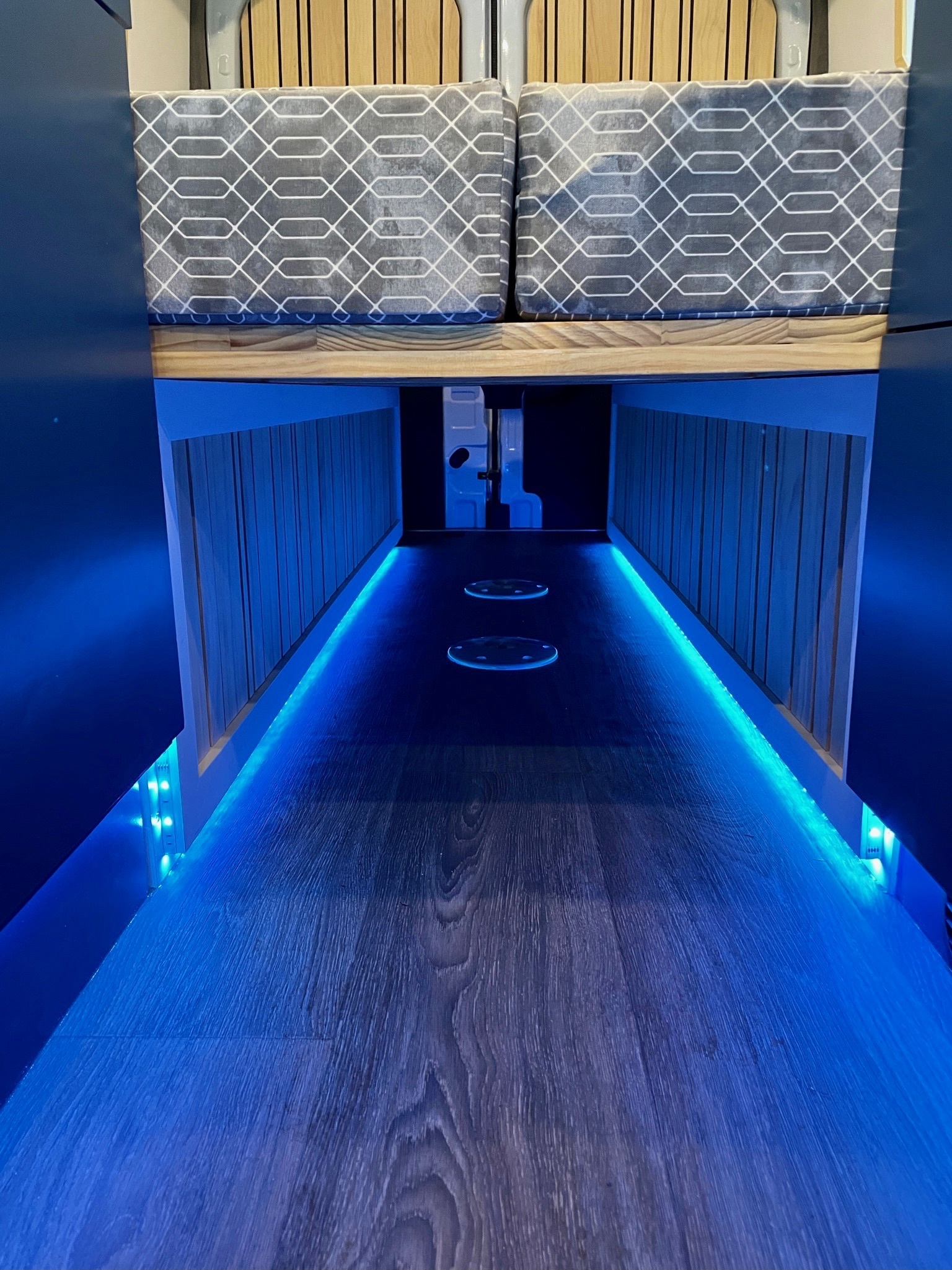 Modern RV rental interior: wood-look floor, comfortable bed, and striking blue LED ambient lighting line the aisle.. Ford Transit 2020