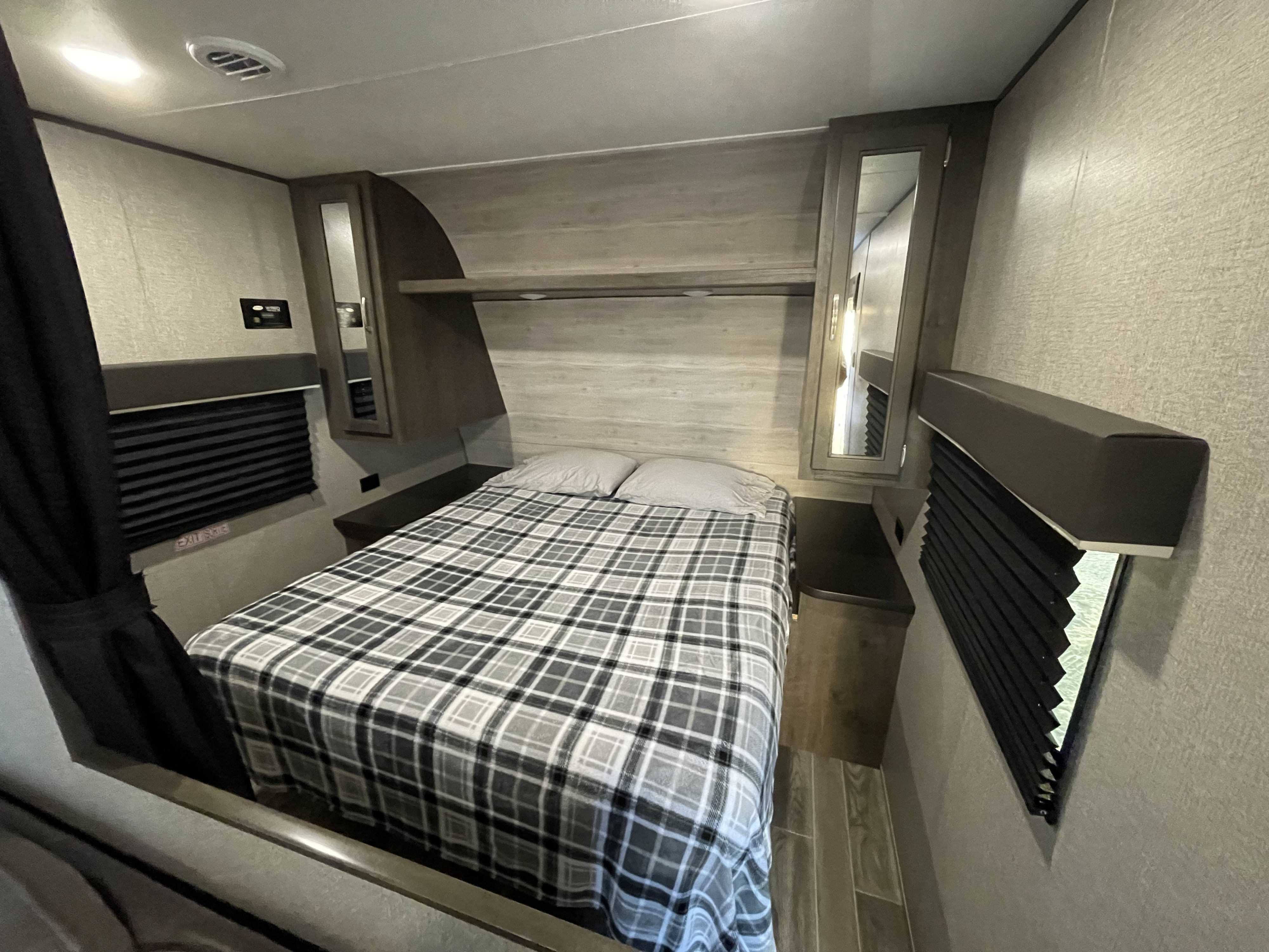 Cozy RV rental bedroom with a grey plaid bed, overhead cabinets, and window blinds for comfortable travel.. Jayco Jay Flight 2021