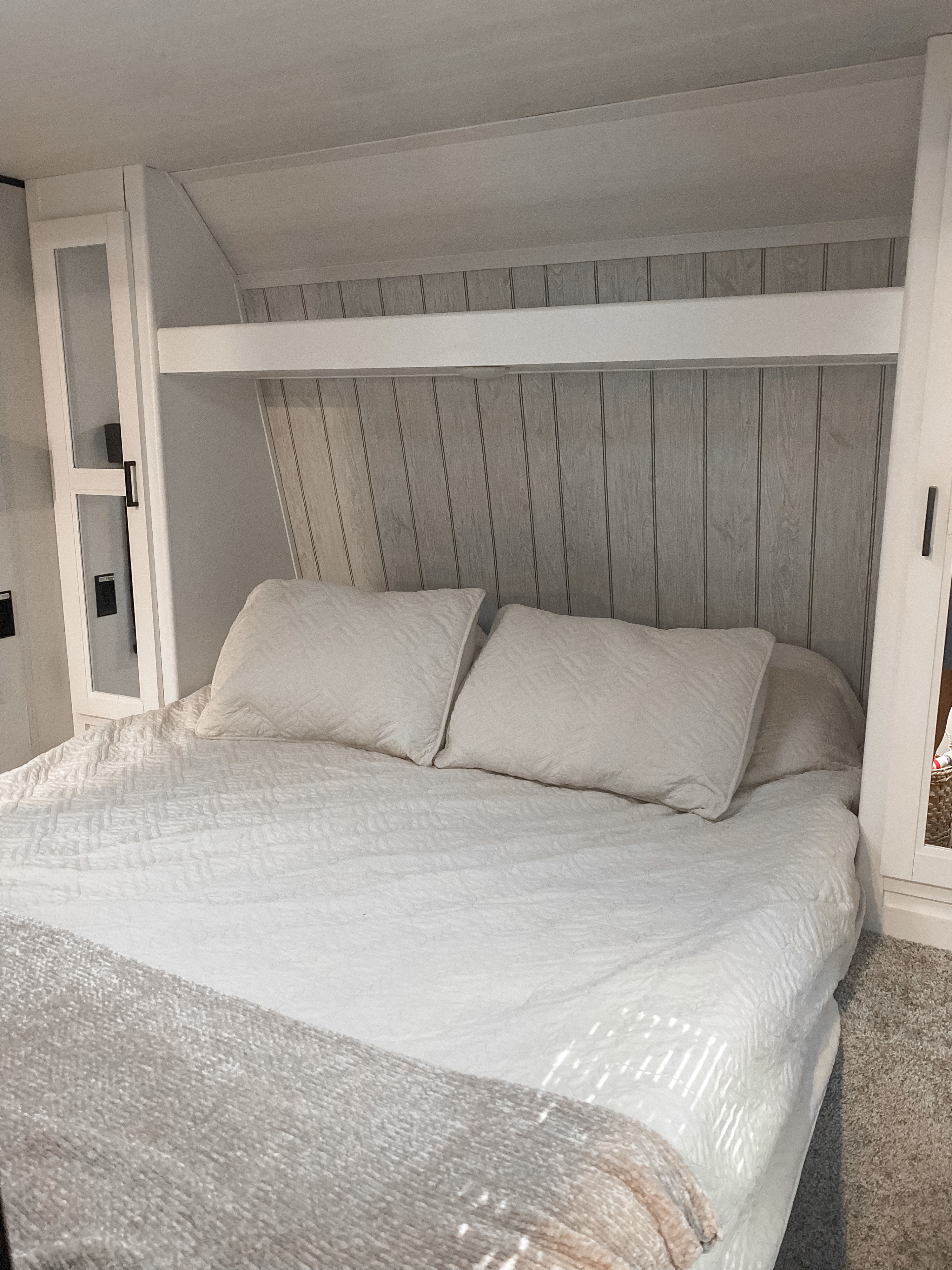 Cozy RV rental bedroom with a white bed, pillows, and stylish wood-paneled headboard featuring built-in storage.. Keystone RV Hideout 2022