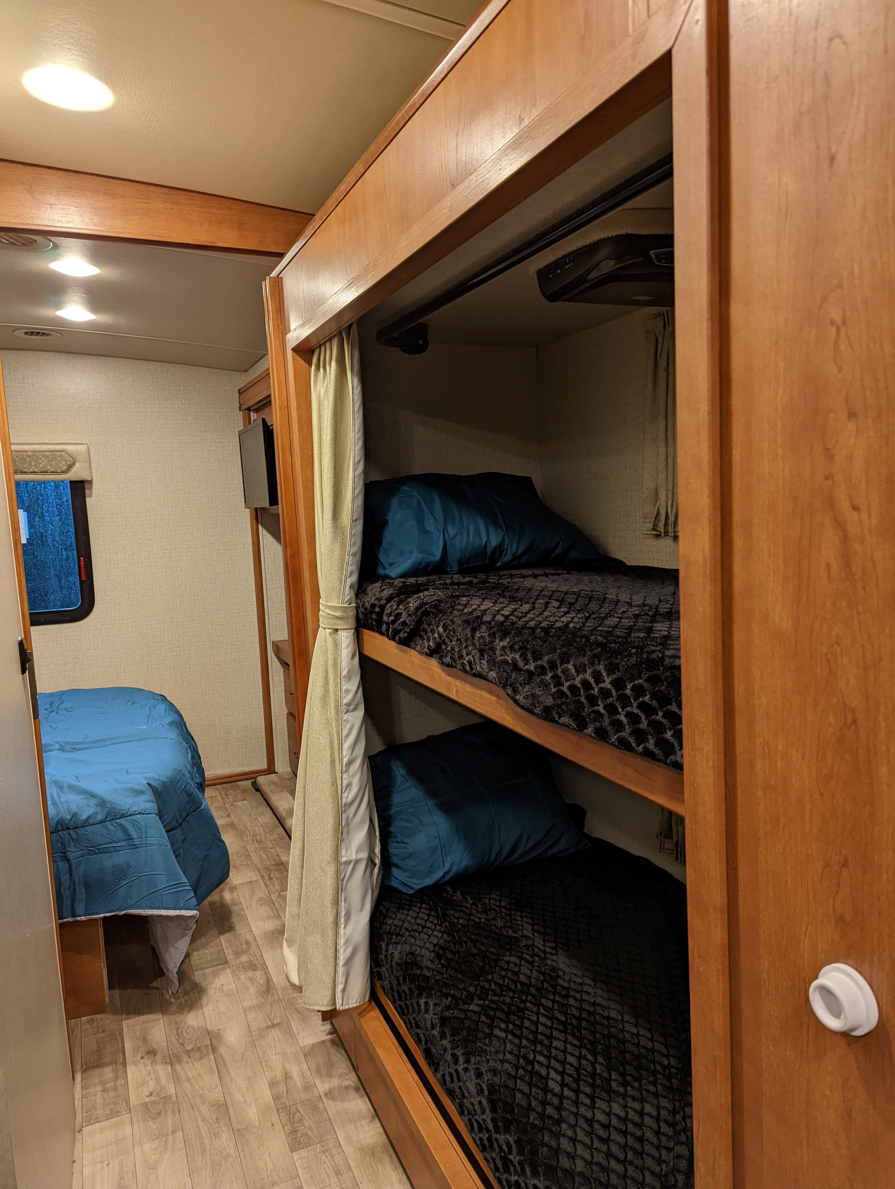 Interior of an RV rental featuring built-in bunk beds with blue pillows and black blankets, and a main bed with a blue comforter.. Winnebago Vista 2018