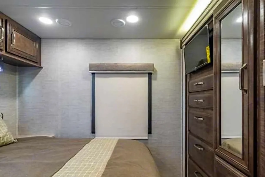 Modern RV rental bedroom with bed, wall-mounted TV, window shade, and built-in storage for comfortable travel.. Entegra Coach Esteem 2021
