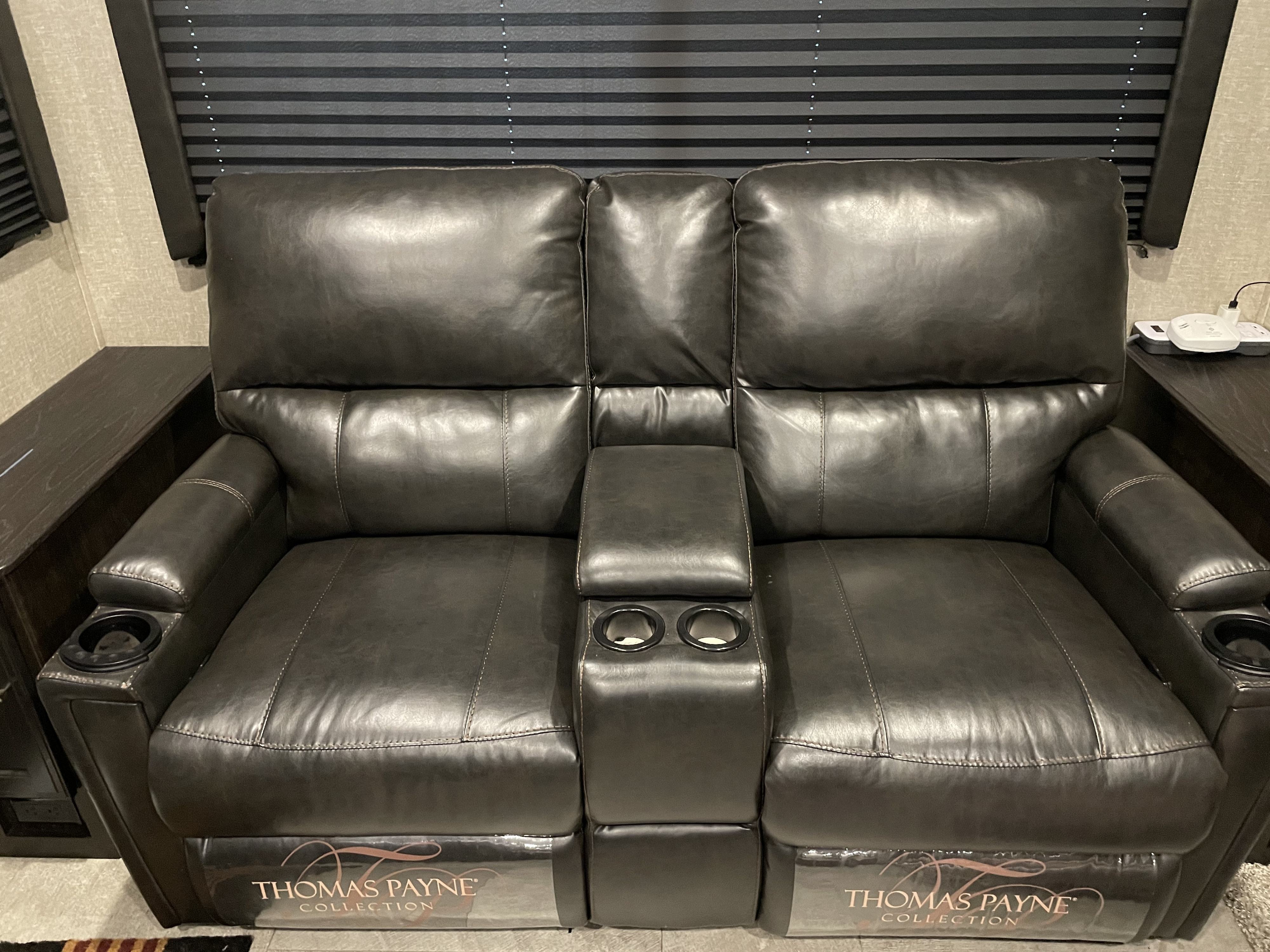 A plush, dark leather Thomas Payne recliner with dual cupholders and side tables, typical in an RV rental.. Grand Design Imagine 2019