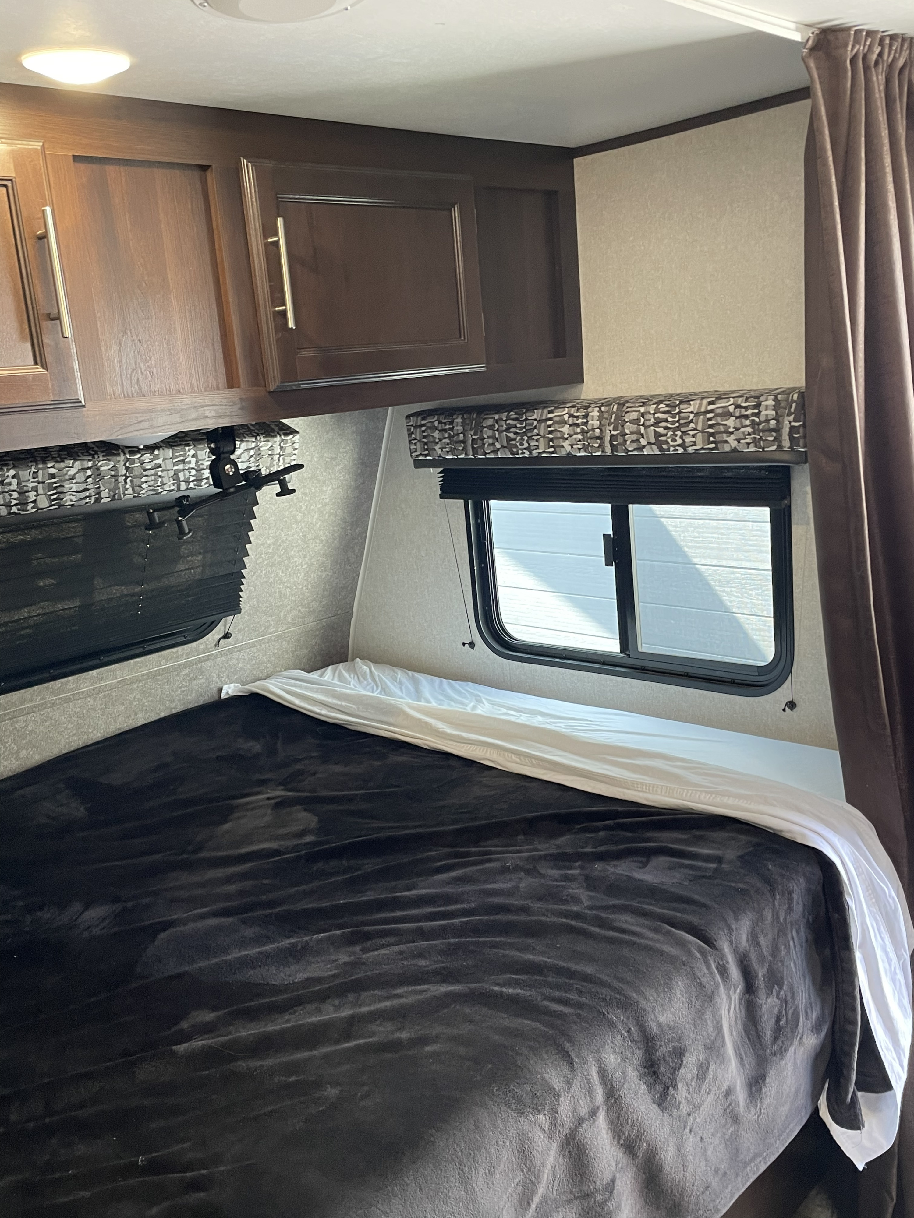 RV rental bedroom: a comfortable space with dark bedding, wooden cabinets, and a window.. Jayco Jay Flight SLX Baja Edition 2019
