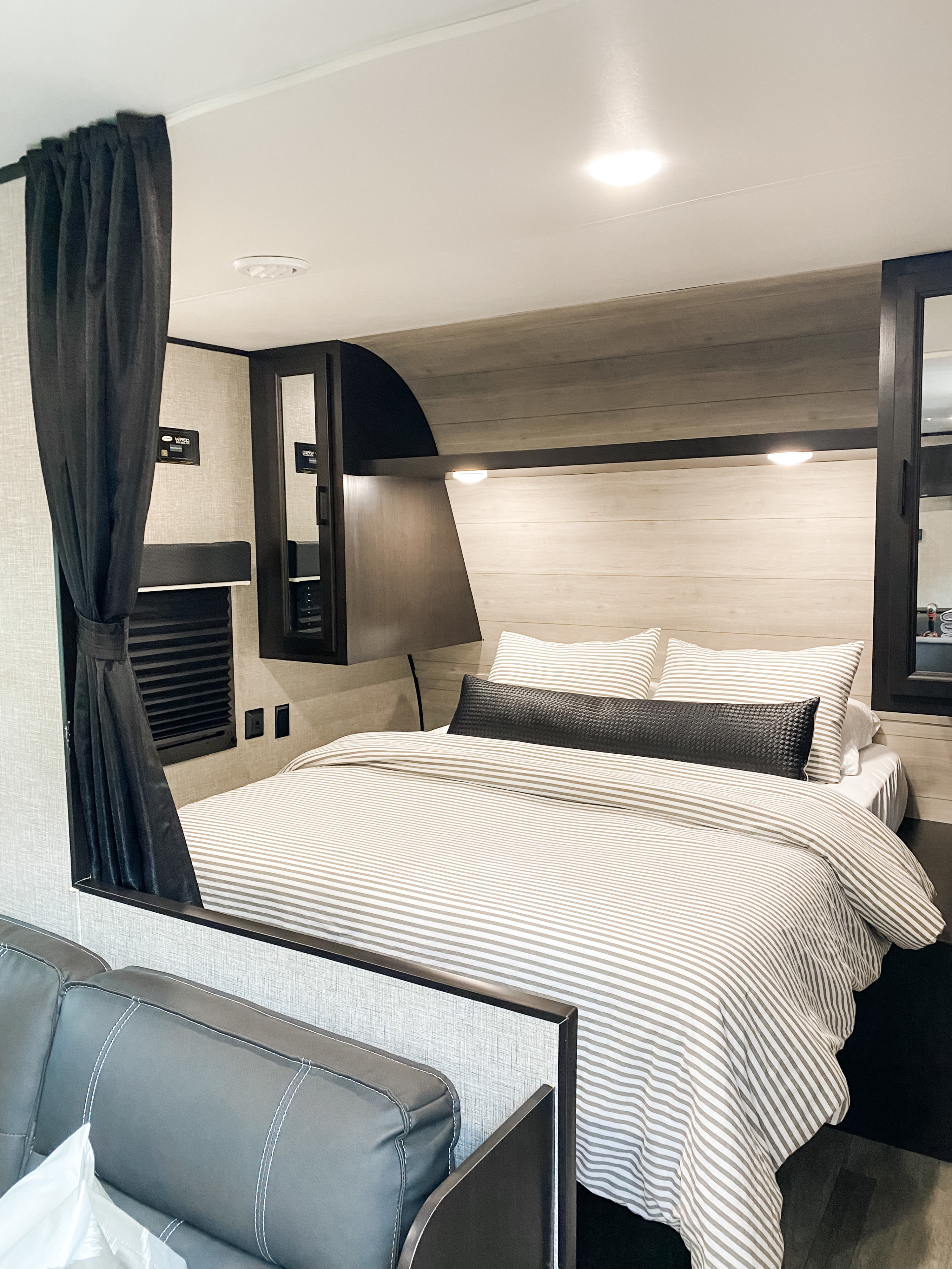 This RV rental features a cozy bedroom with a striped bed, dark cabinetry, light wood walls, and a dark curtain for privacy.. Jayco Jay Flight SLX 2022