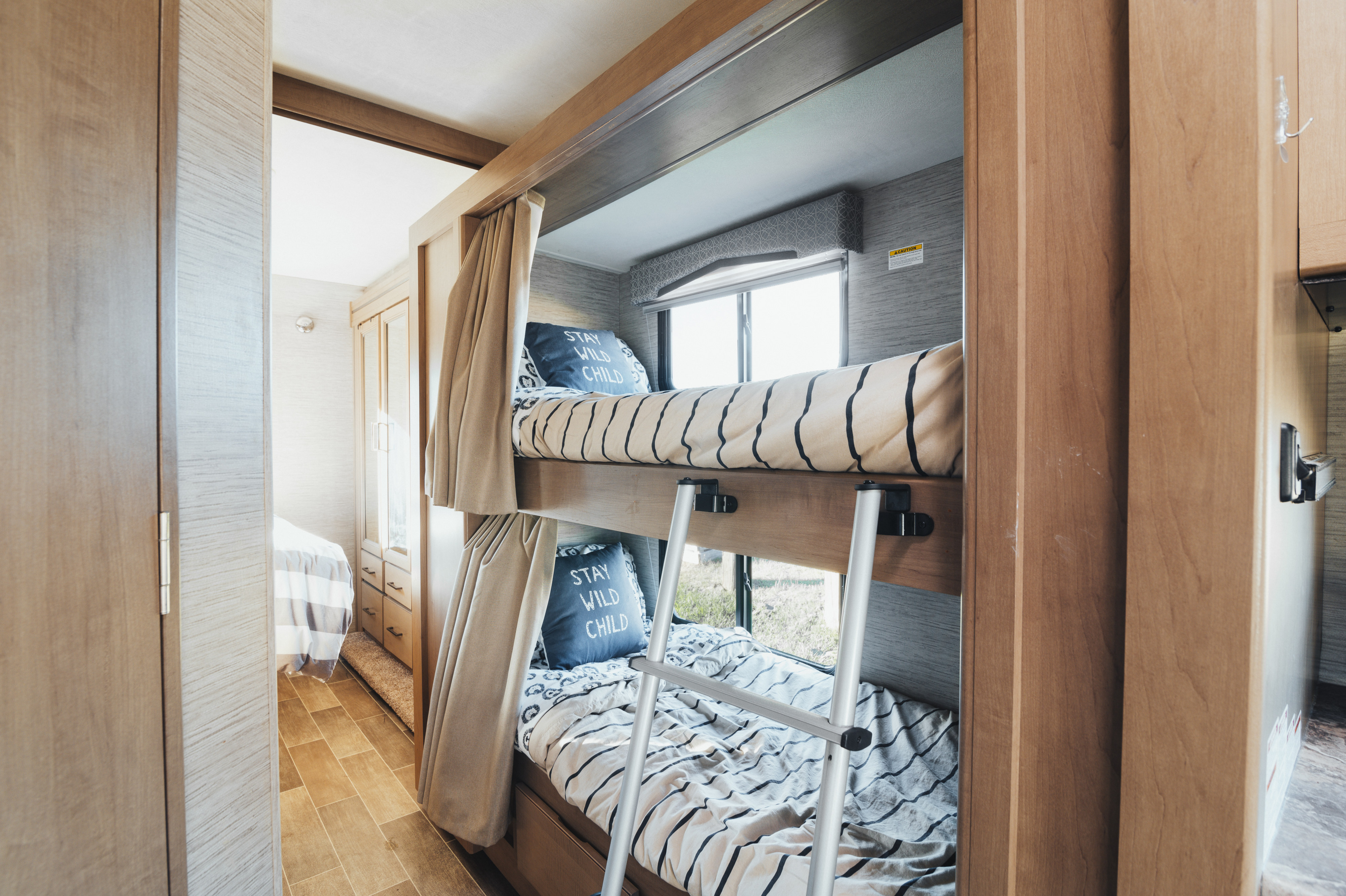 Cozy RV rental interior with bunk beds featuring "Stay Wild Child" pillows, ideal for family adventures on the road.. Thor Chateau 2022