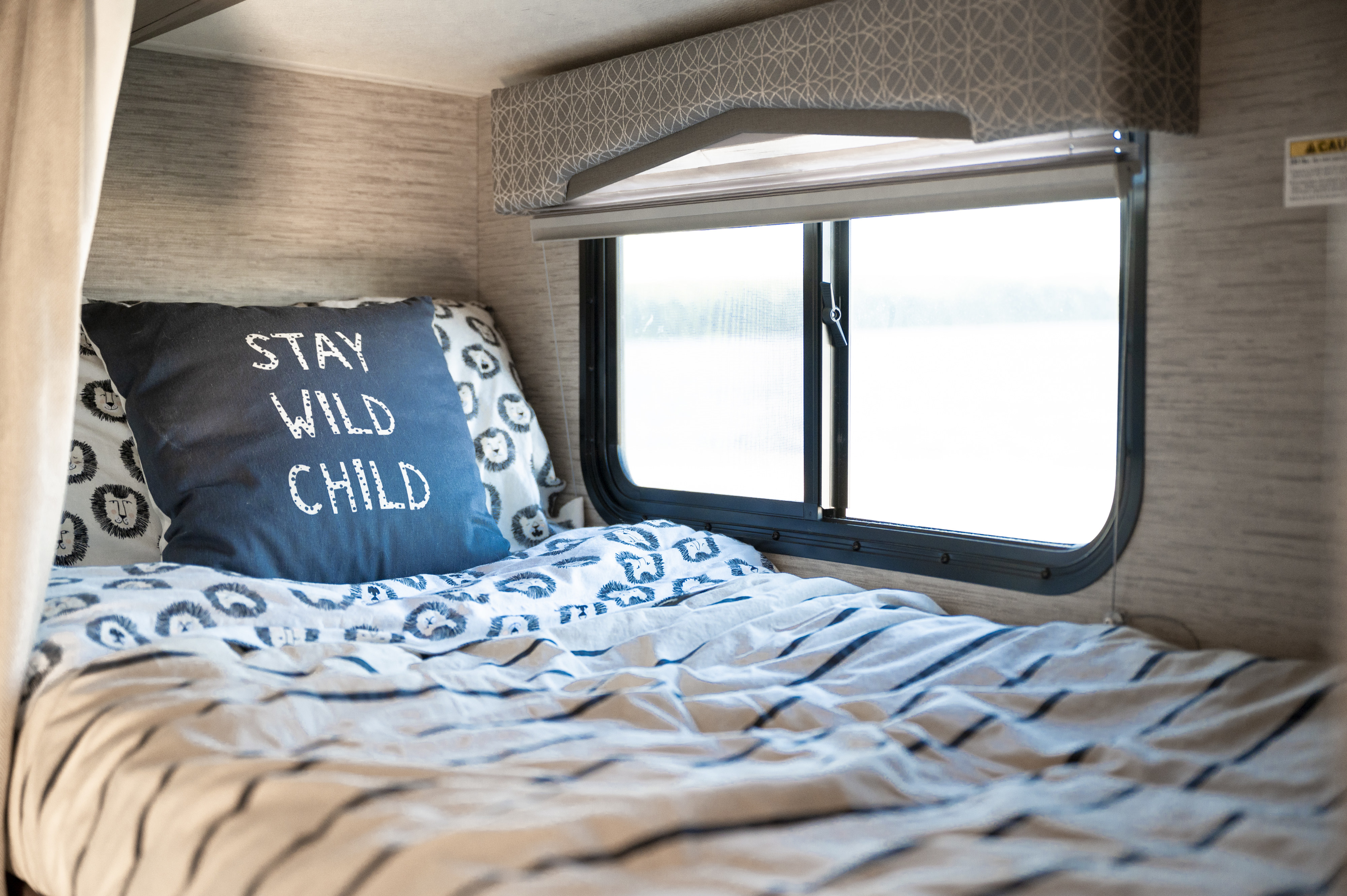 Cozy RV rental bed with "STAY WILD CHILD" pillow and lion print bedding. Perfect for adventurous family travel.. Thor Chateau 2022