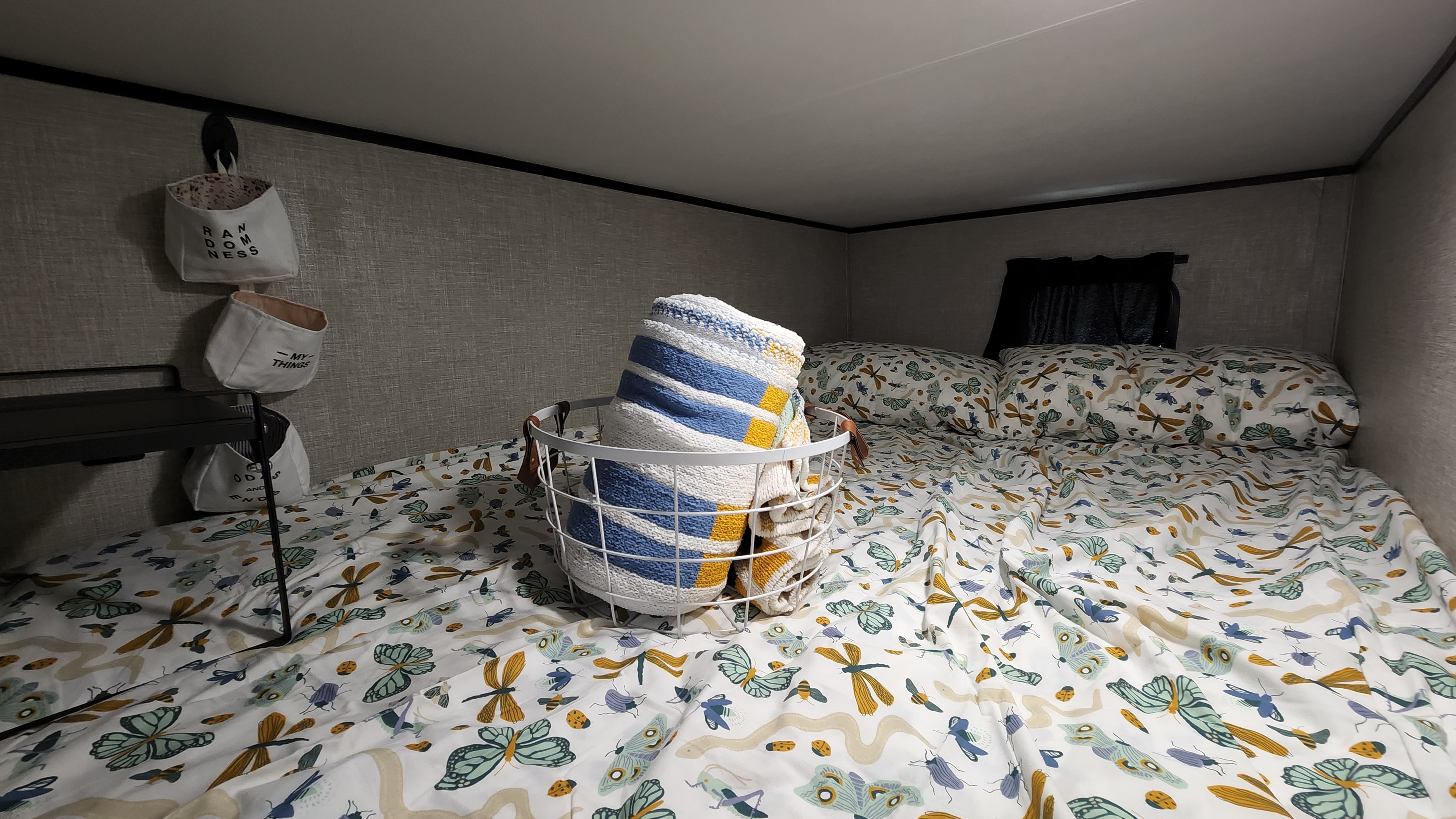 Cozy RV rental bunk bed with insect-patterned bedding, a rolled blanket, and wall storage baskets for a comfortable stay.. Jayco Jay Flight SLX 2022