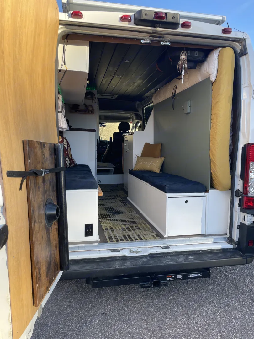 Inside this comfy RV rental camper van, seen from the rear. Features custom built-ins, seating/beds, and storage for van life adventures.. Ram Promaster 2500 2019