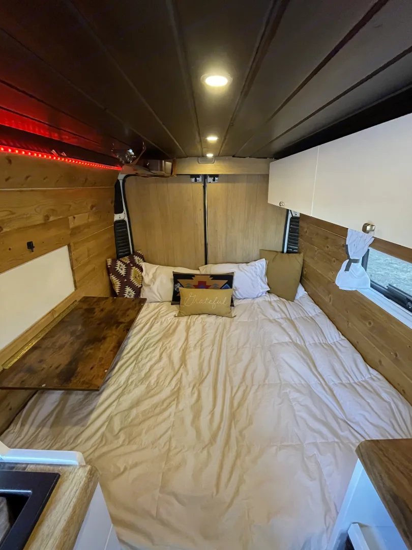 Spacious RV rental interior with a large bed, wood paneling, and ambient lighting, offering a cozy mobile living space.. Ram Promaster 2500 2019