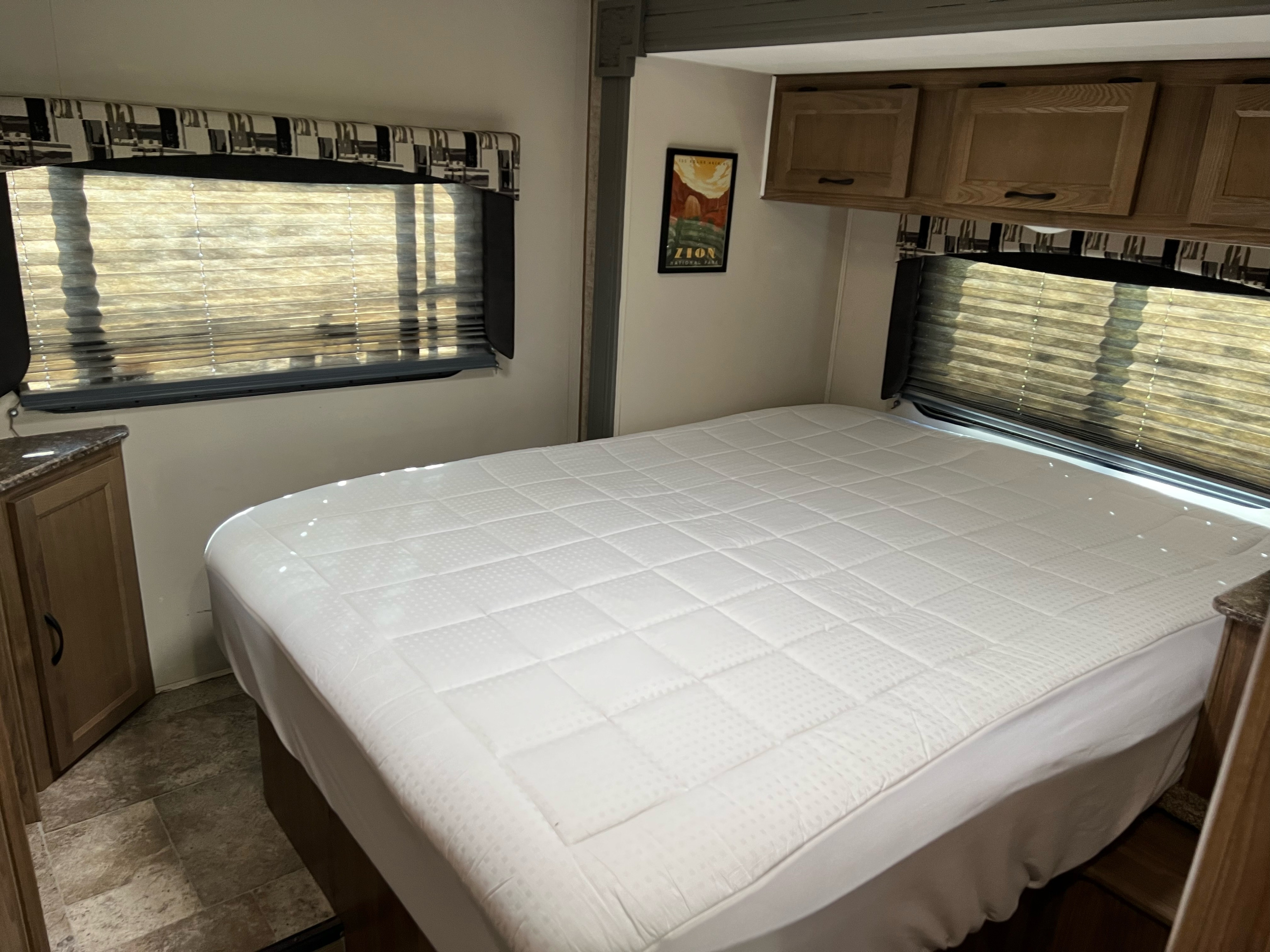 RV rental bedroom with a white bed and quilted mattress pad, window blinds, wooden cabinets, and a Zion poster.. Forester GTS 2017