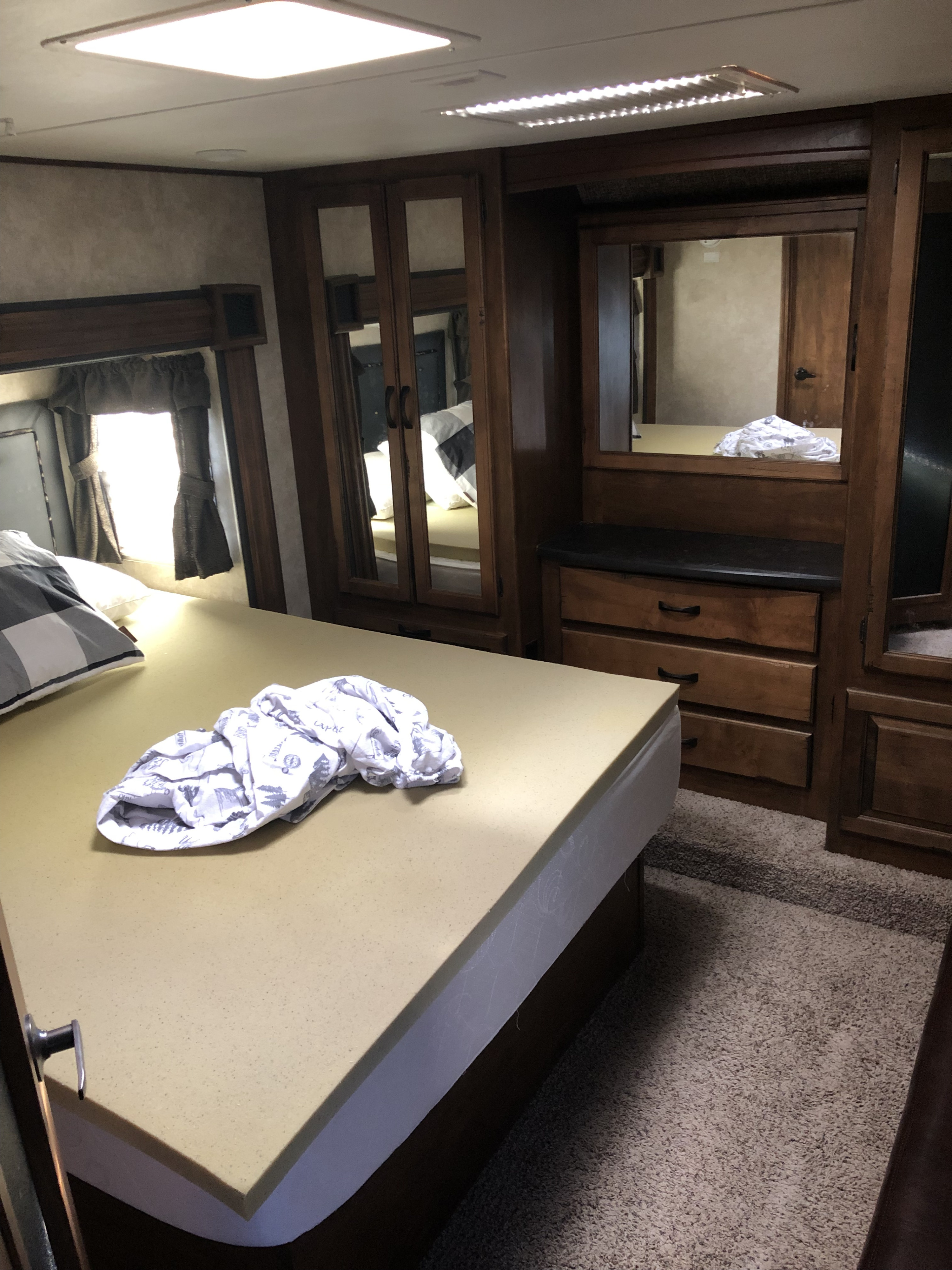 RV rental bedroom with a large bed, built-in wood cabinets, dresser, window, and carpeted floor.. Keystone Raptor 2014